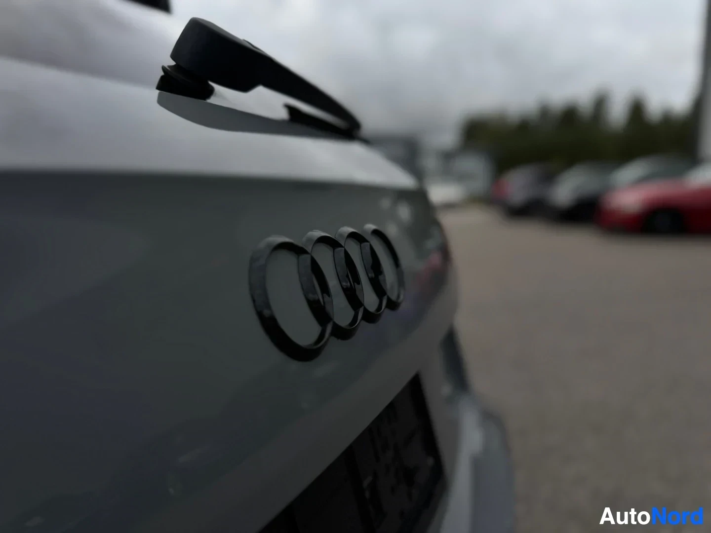Yksityiskohta: Lähikuva auton takaluukusta, jossa on Audi-logo ja takalasinpyyhin. Logo on musta.