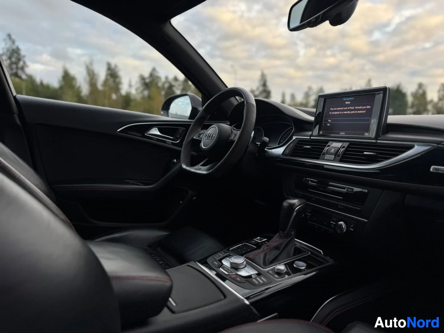 Ohjaamo: Kuvakulma etumatkustajan puolelta näyttäen ohjaamon, kojelaudan ja keskikonsolin. Infotainment-näytöllä on tekstiä.