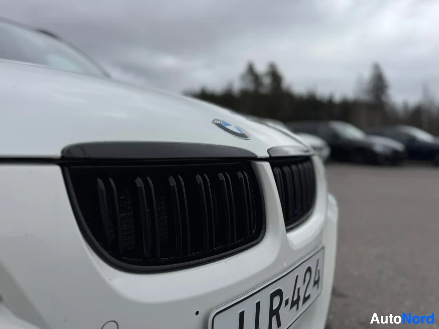 Edestä: Lähikuva valkoisen auton mustasta etusäleiköstä, jossa on BMW-logo. Eturekisterikilpi on osittain näkyvissä.
