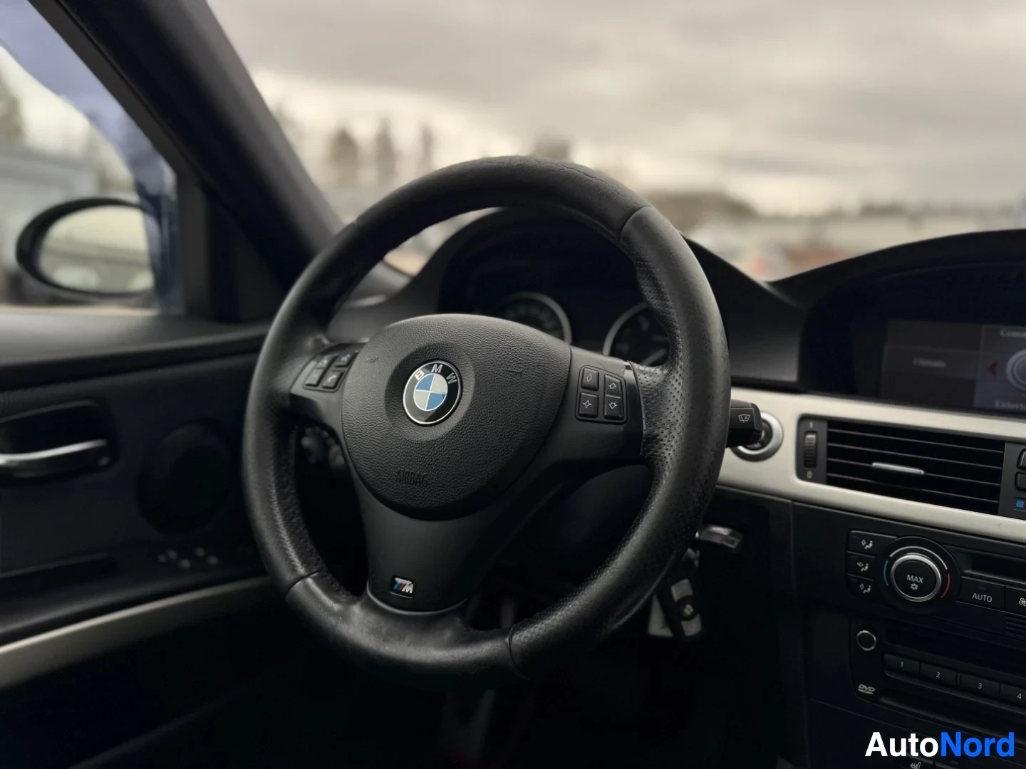 Yksityiskohta: Lähikuva auton ohjauspyörästä, jossa on BMW-logo ja monitoiminäppäimet.