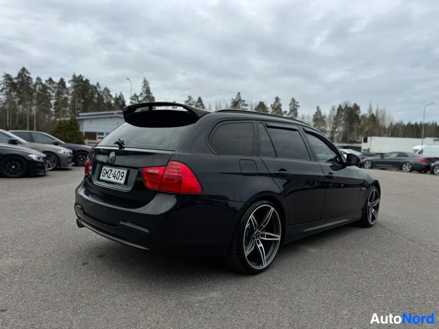 Takaviisto: Musta farmariauto on pysäköity ulos ja kuvattu takavasemmalta. Auto seisoo asfaltilla ja sen takaluukussa on spoilerit.
