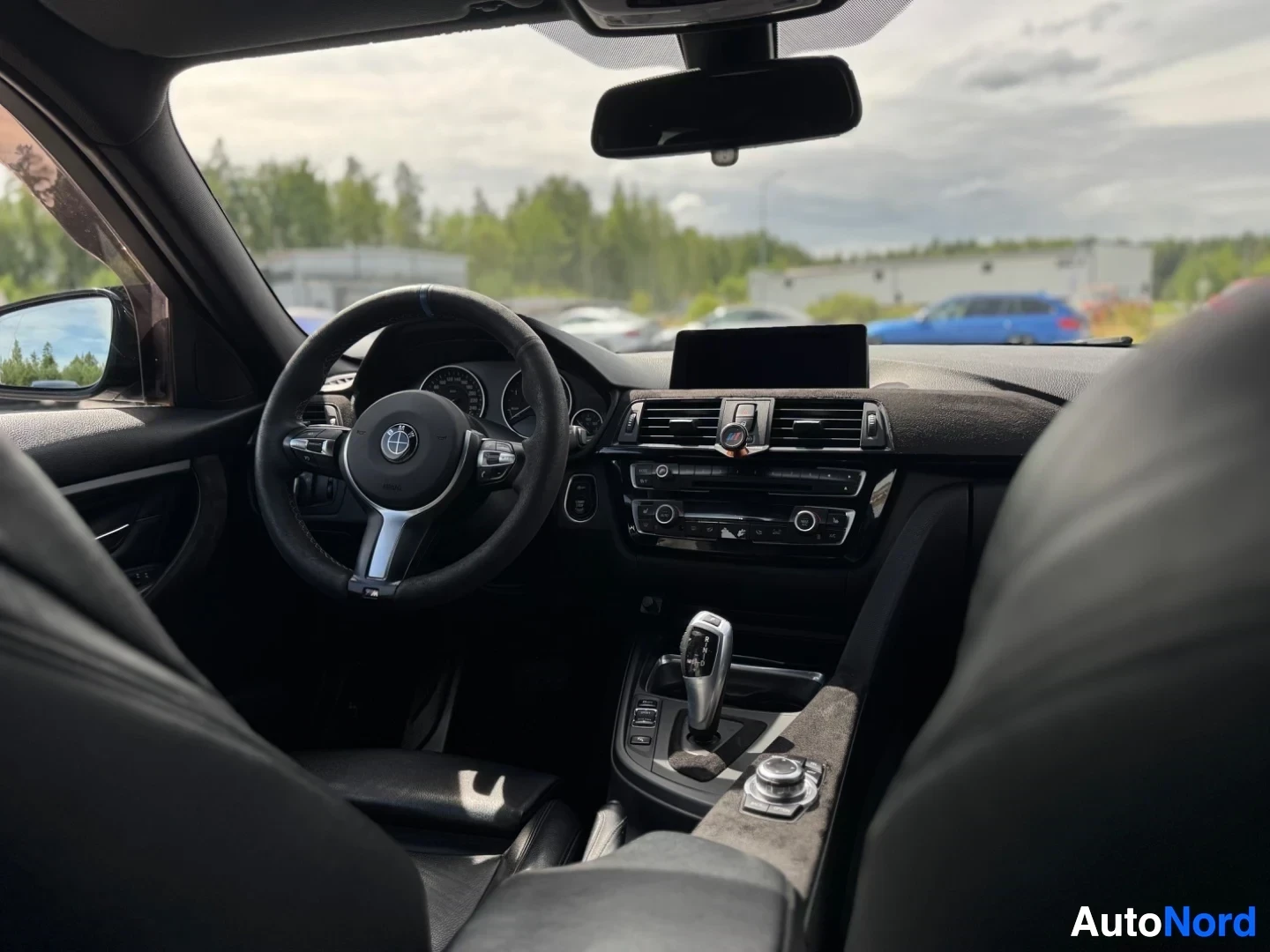 Ohjaamo: Sisäkuva autosta edestäpäin, tummat istuimet ja ohjaamo, jossa keskellä näyttö ja vaihdekeppi.