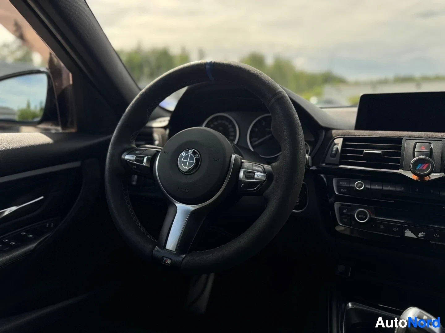 Yksityiskohta: Lähikuva ohjauspyörästä, jossa on BMW-logo keskellä ja M-logo alareunassa. Mittaristo näkyy ohjauspyörän takana.