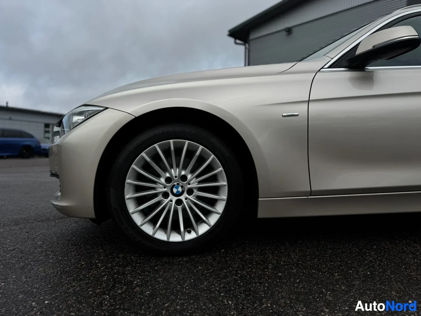 Etuviisto, nokka vasemmalle: Lähikuva beigen värisen auton etuosasta ja vasemmasta etupyörästä. Pyörässä on hopeinen monipuolavanne, jossa on BMW-logo.