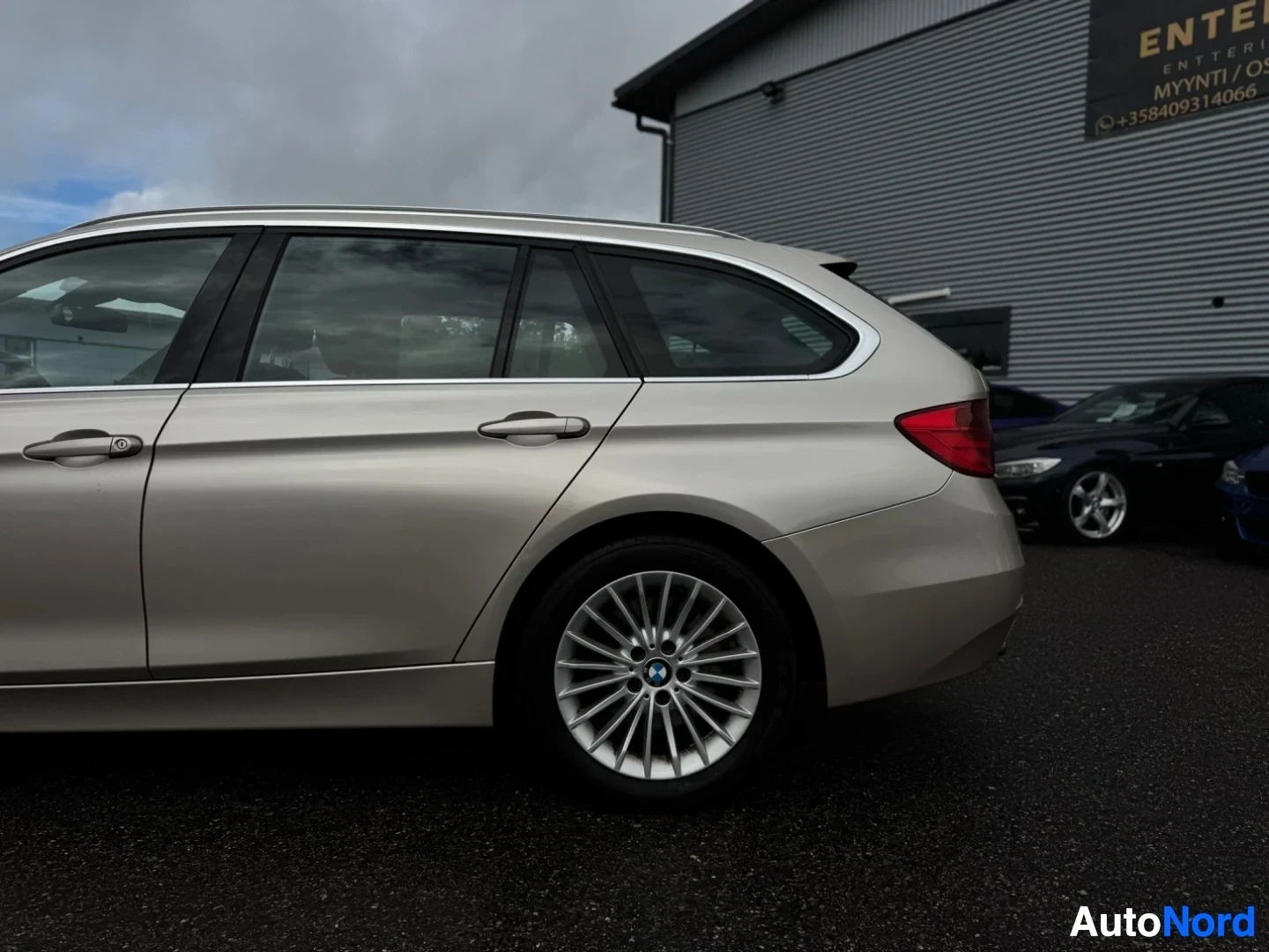 Takaviisto: Lähikuva beigen värisen farmariauton oikeasta takaosasta ja takapyörästä. Pyörässä on hopeinen monipuolavanne, jossa on BMW-logo. Ikkunoissa on tummennukset.