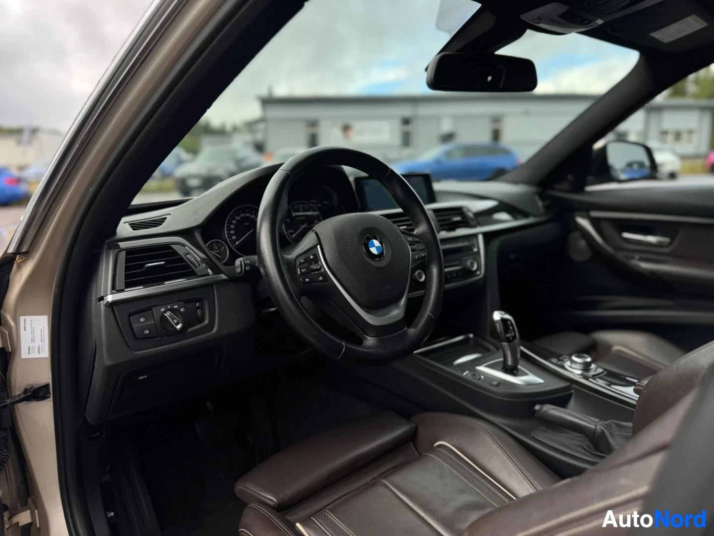 Ohjaamo: Kojelaudan ja ohjauspyörän lähikuva. Ohjauspyörässä on monitoiminäppäimet ja keskellä BMW-logo. Vaihdekeppi ja tietoviihdejärjestelmän säädinnäppäimet näkyvät k