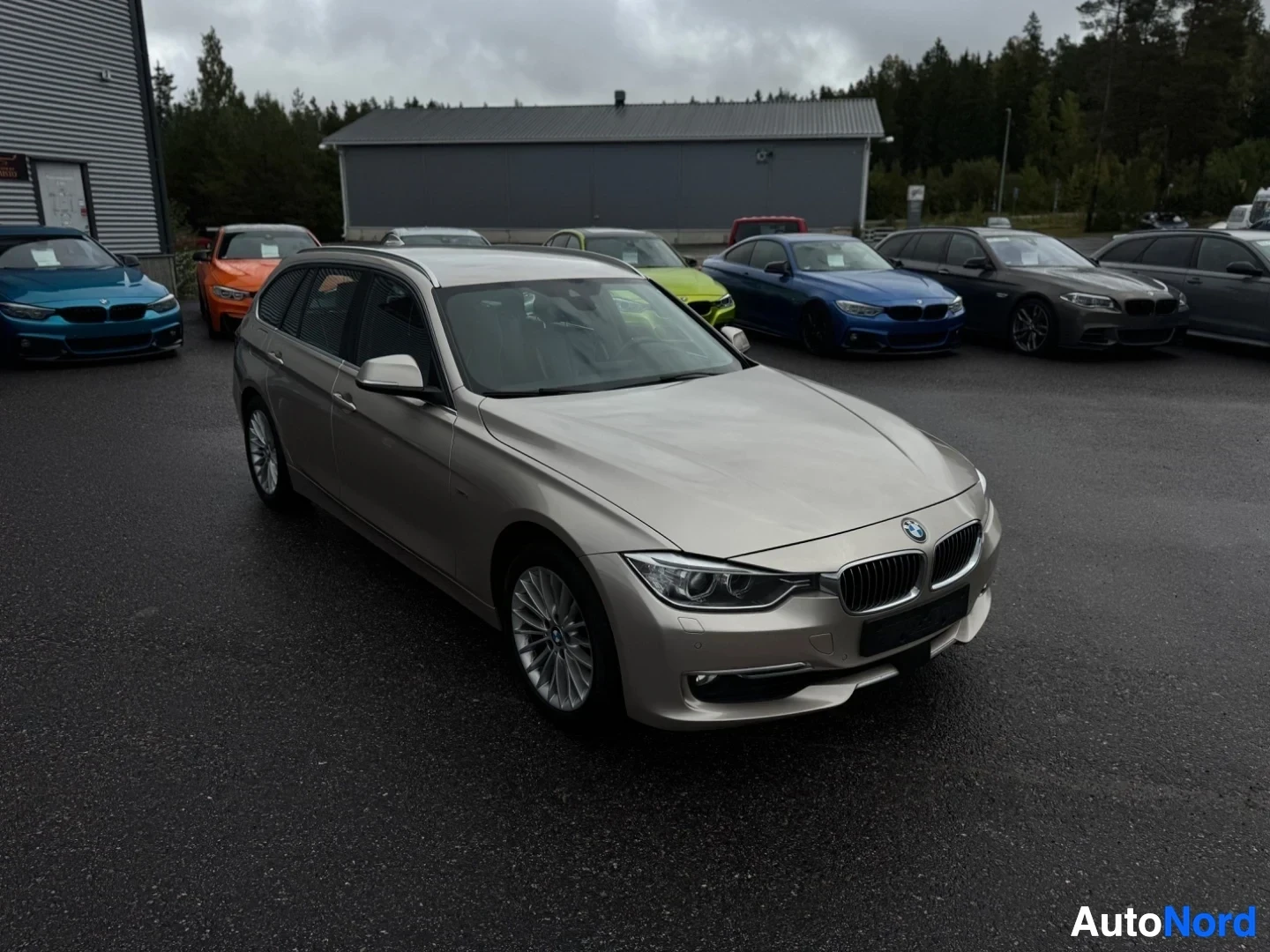 Etuviisto, nokka oikealle: Beigen värinen farmariauto pysäköitynä muiden autojen eteen myymälän eteen. Ajoneuvossa on monipuolaiset kevytmetallivanteet ja krominvärisiä yksityiskoh