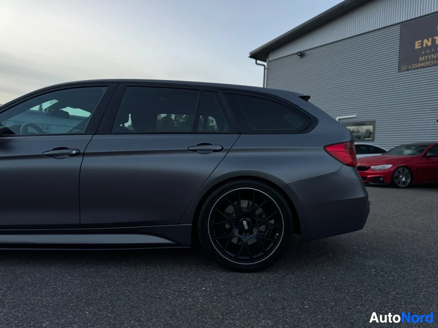 Takaviisto: Mattaharmaa farmariauto on pysäköity ulos rakennuksen eteen. Auto on kuvattu oikealta takaviistosta.