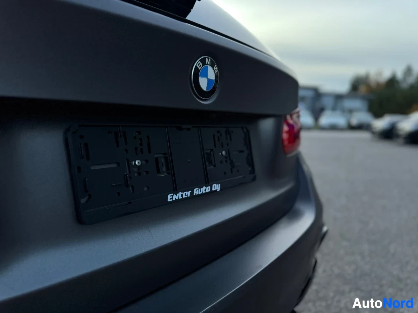 Takaviisto: Lähikuva auton perästä, jossa näkyy tyhjä rekisterikilven alusta tekstillä "Enter Auto Oy" ja BMW-logo takaluukussa.