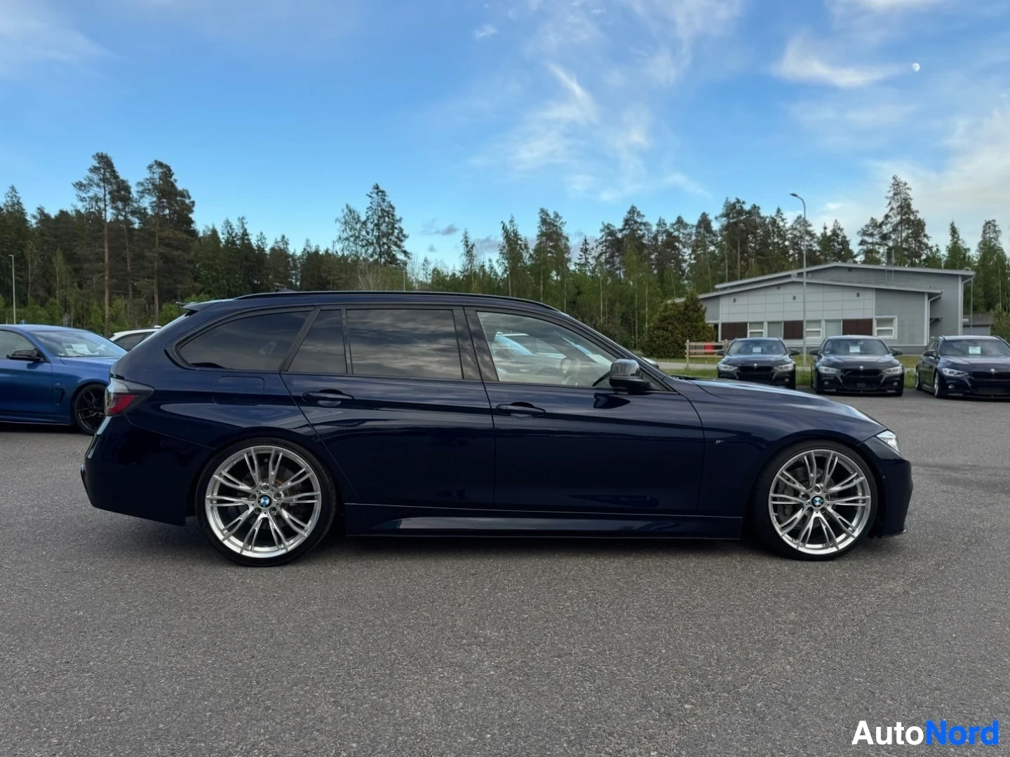 Sivulta: Sivukuva tummansinisestä farmarimallin henkilöautosta, joka on pysäköity ulkona asfalttikentällä. Autossa on kattokaiteet ja monipuolaiset kevytmetallivanteet.