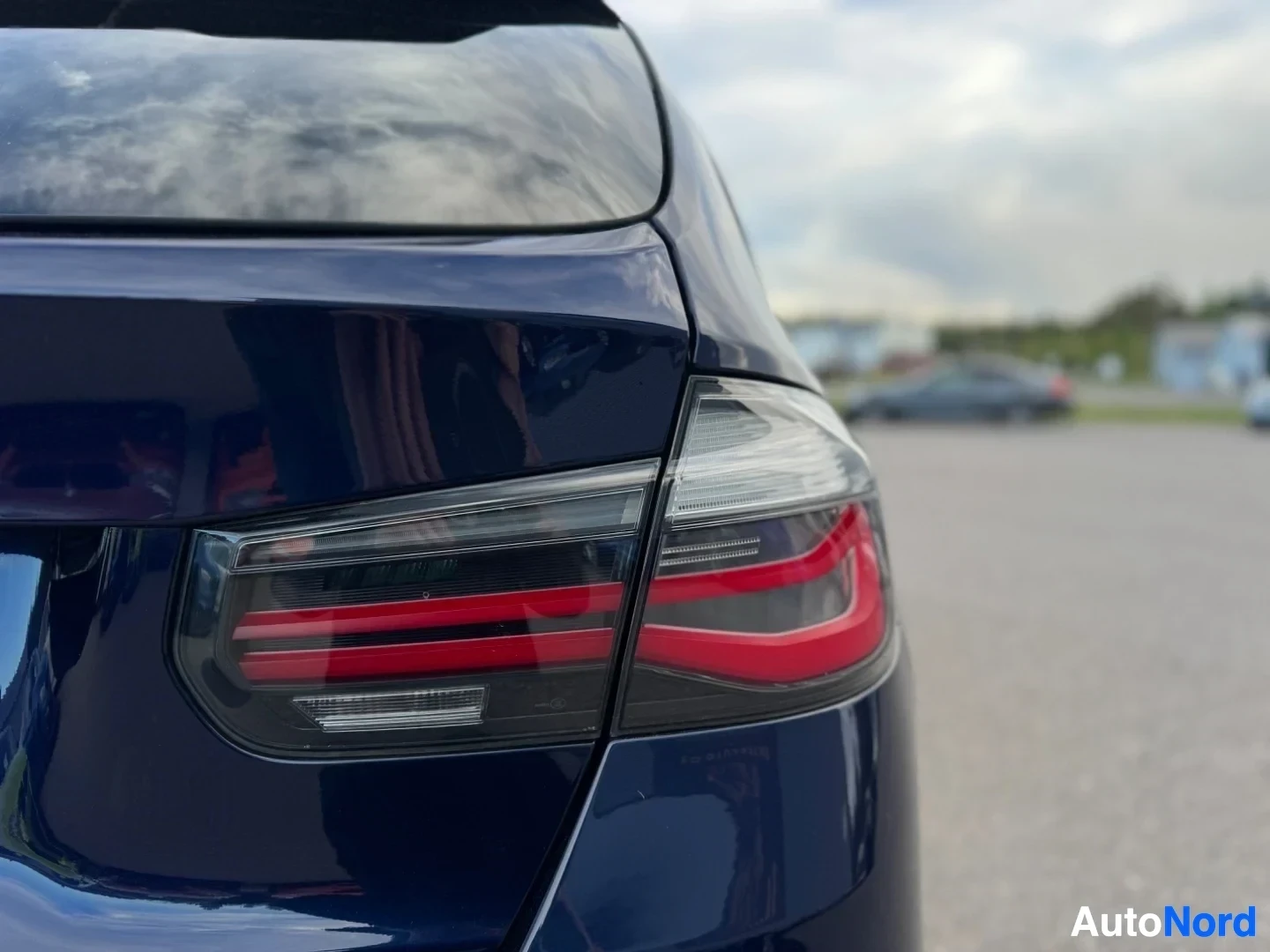 Yksityiskohta: Lähikuva auton vasemmasta takavalosta, jossa on punaisia ja valkoisia LED-valojuovia. Auto on tummansininen ja seisoo asfalttiparkkipaikalla.