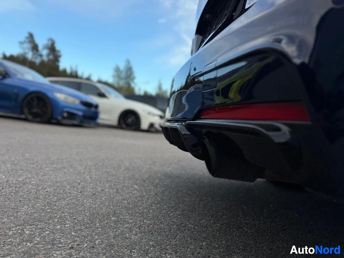 Takaviisto: Kuva auton takapuskurin alaosasta, jossa näkyy neljä pakoputken ulostuloa. Auto on tummansininen ja kuvattu matalasta kuvakulmasta asfalttipinnalta.