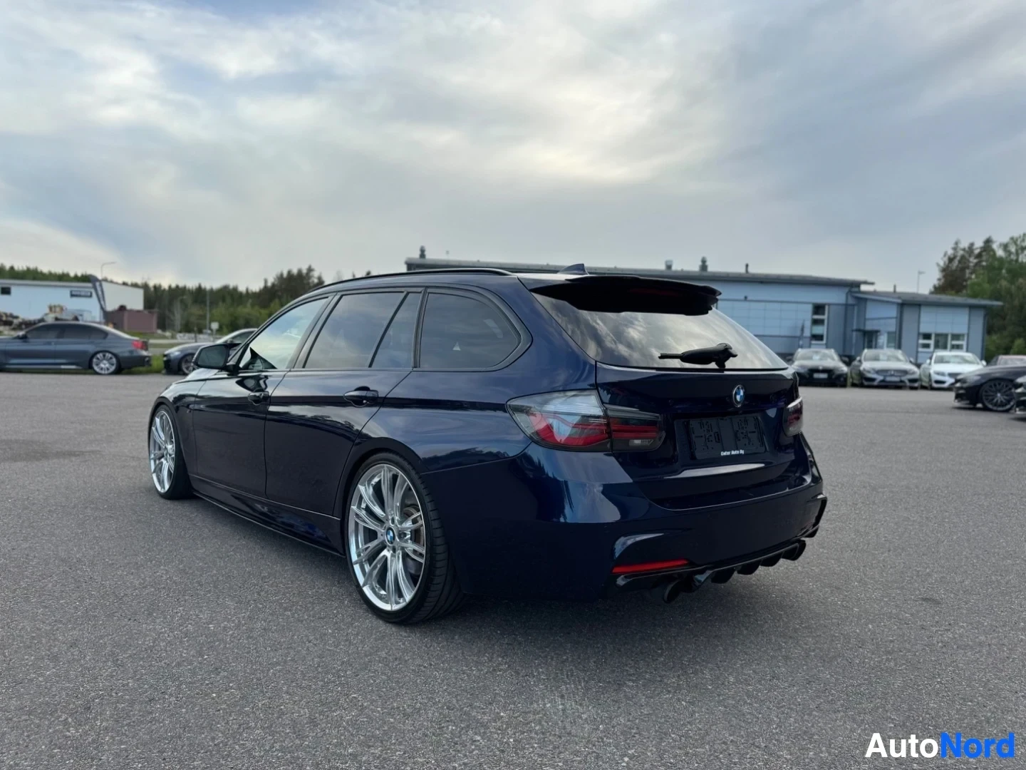 Takaviisto: Tummaninsininen farmariauto takaviistosta kuvattuna. Autossa on tummennetut takalasit ja kiiltävät kevytmetallivanteet. Takana näkyy kaksi pakoputken ulostuloa