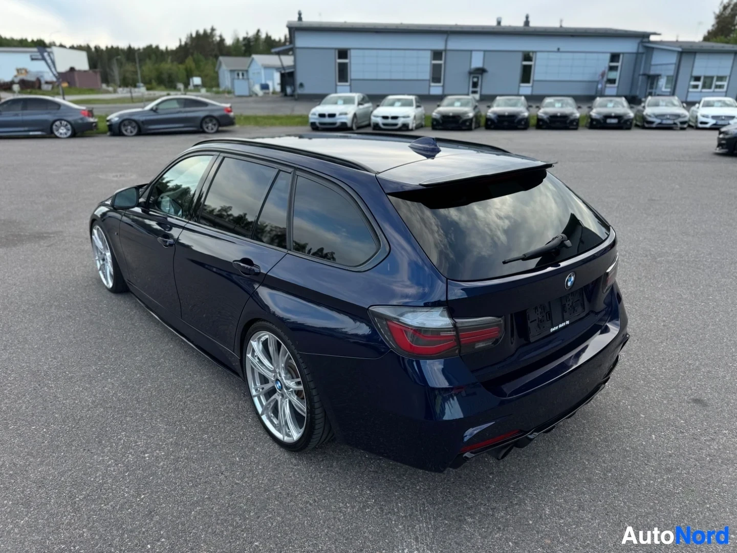 Takaviisto: Tummaninsininen farmariauto takaviistosta yläpuolelta kuvattuna. Autossa on kattokiskot ja takaluukussa pieni spoileri. Takavalot ovat näkyvissä. Parkkipaikalla