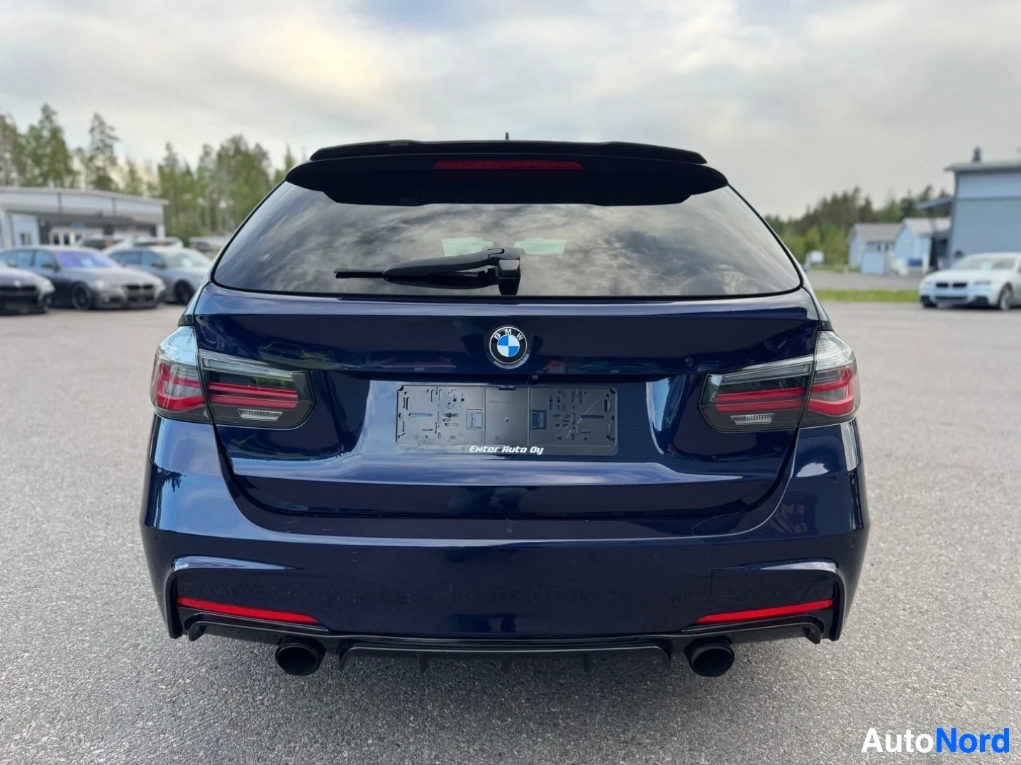 Takaa: Tummanpunainen BMW-farmariauto takaa kuvattuna, takaikkunan pyyhin on pystyasennossa. Takaluukussa on hopeinen BMW-logo ja alareunassa kaksi pakoputkea.