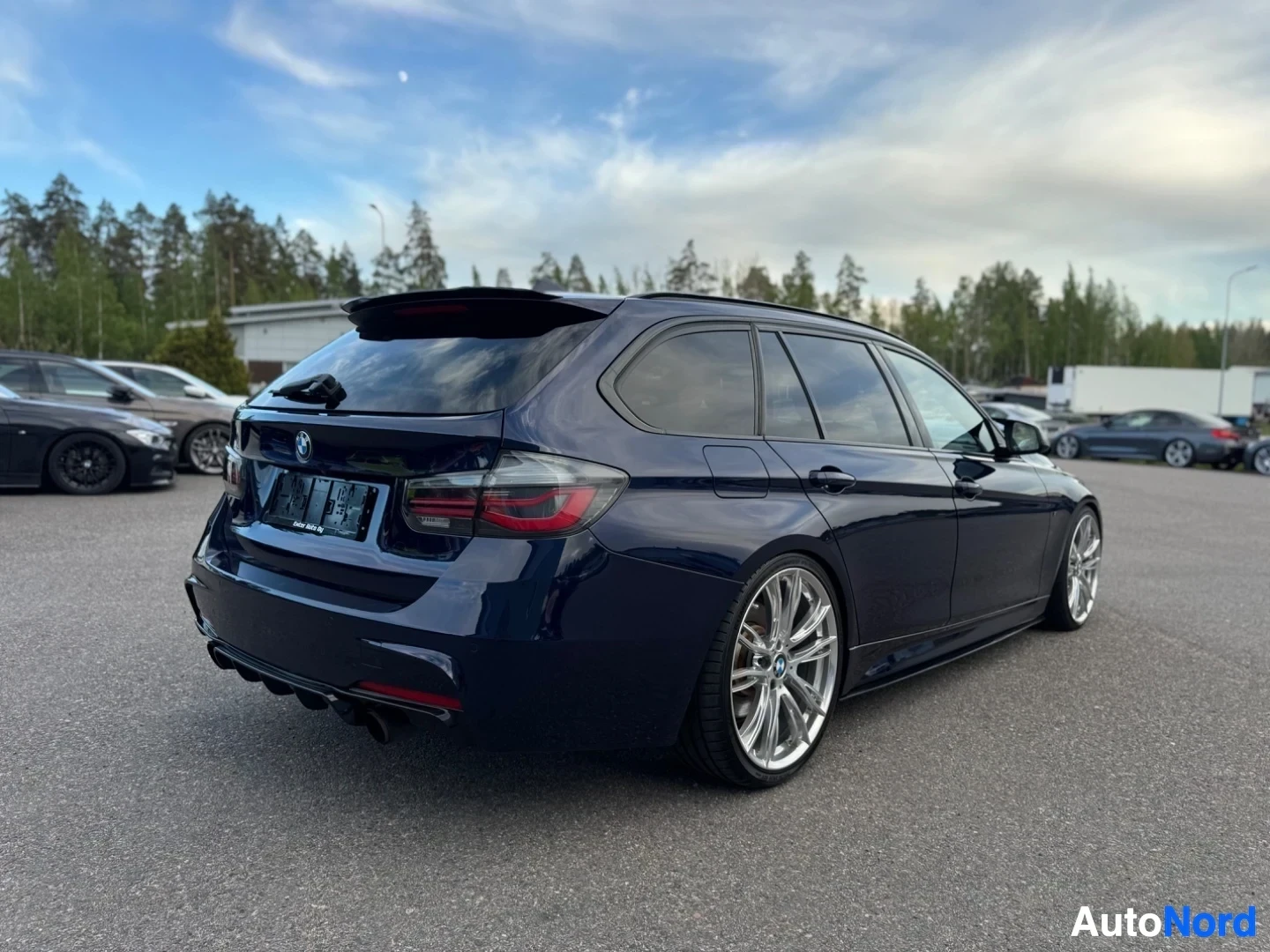 Takaviisto: Tummanpunainen BMW-farmariauto oikealta takaviistosta, taustalla näkyy rakennuksia ja puita.