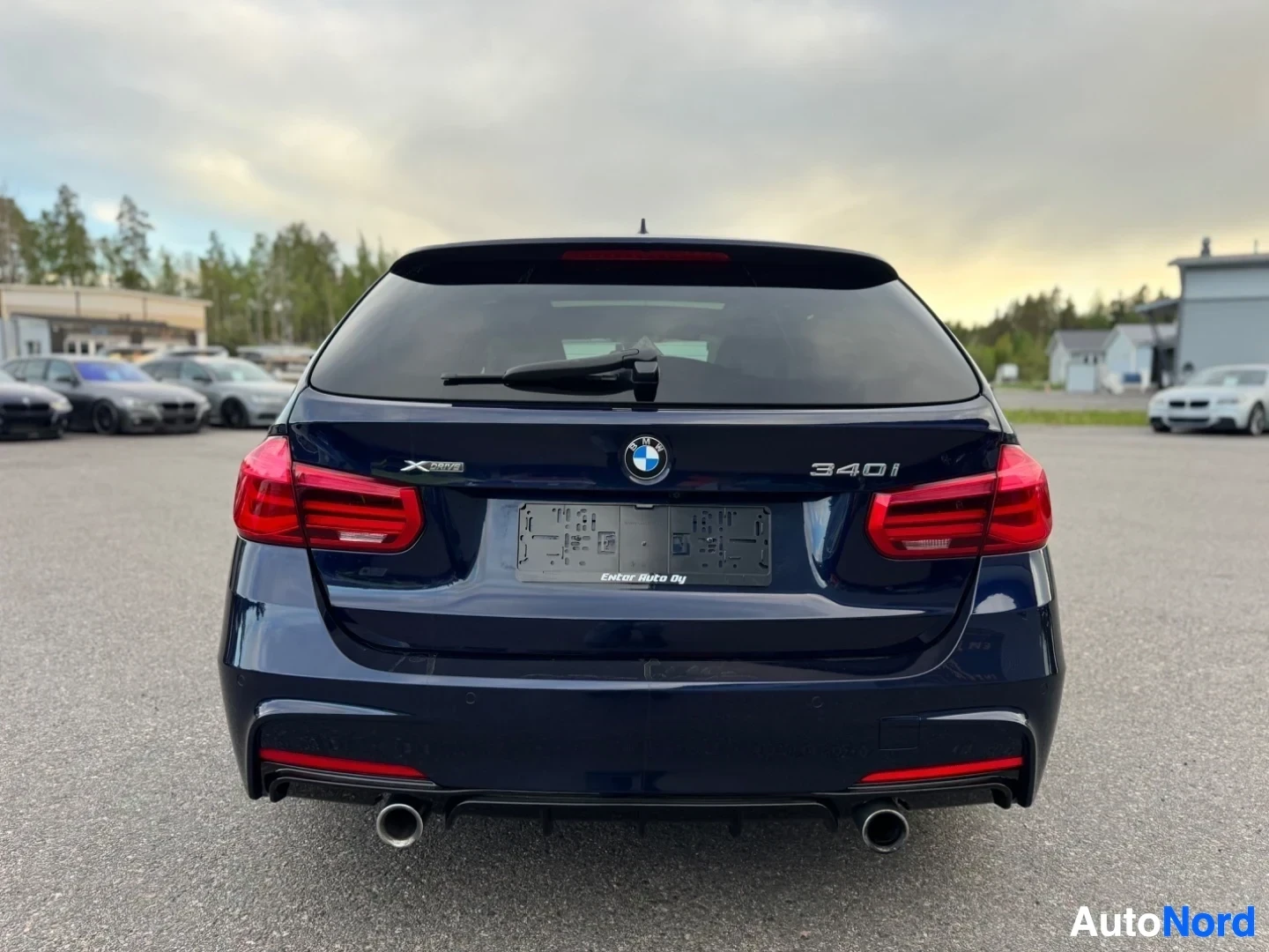 Takaa: Tummanpunaisen BMW-farmariauton peräosa kuvattuna suoraan takaa. Auton takaluukussa lukee "xDrive" ja "340i". Siinä on kaksi pakoputken ulostuloa ja musta rekis