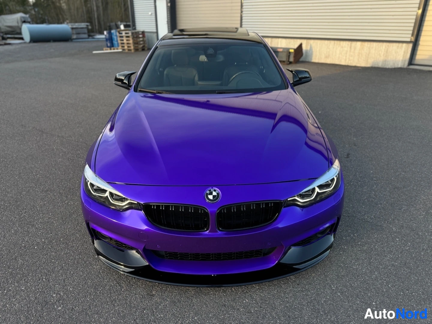 Edestä: Edestä kuvattu violetti BMW-henkilöauto, jossa on musta säleikkö, tummat vanteet ja kiiltävät mustat yksityiskohdat, pysäköitynä pihalle.