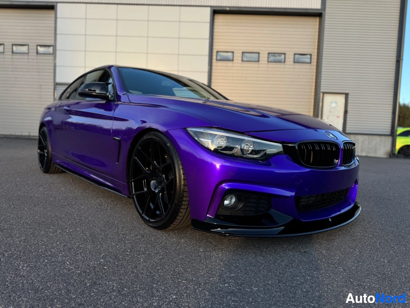 Etuviisto, nokka vasemmalle: Lila BMW-coupé pysäköitynä etuviistosta kuvattuna, ajovalot näkyvissä. Autossa on mustat monipuolaiset kevytmetallivanteet ja musta etupuskurin lippa.