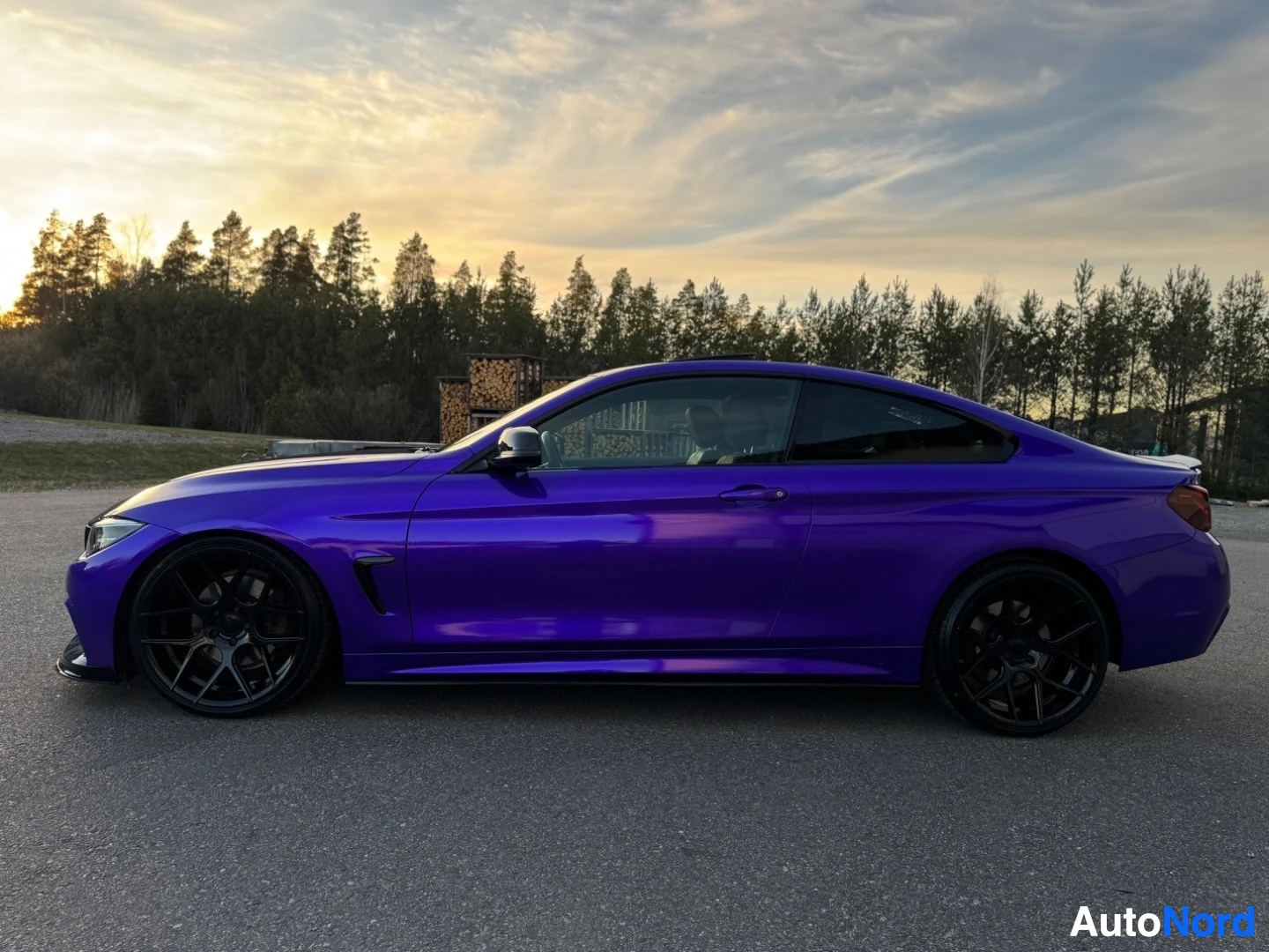 Sivulta: Lila BMW-coupé kuvattuna vasemmalta sivulta profiilista ulkona auringonlaskun aikaan. Autossa on mustat monipuolaiset kevytmetallivanteet.