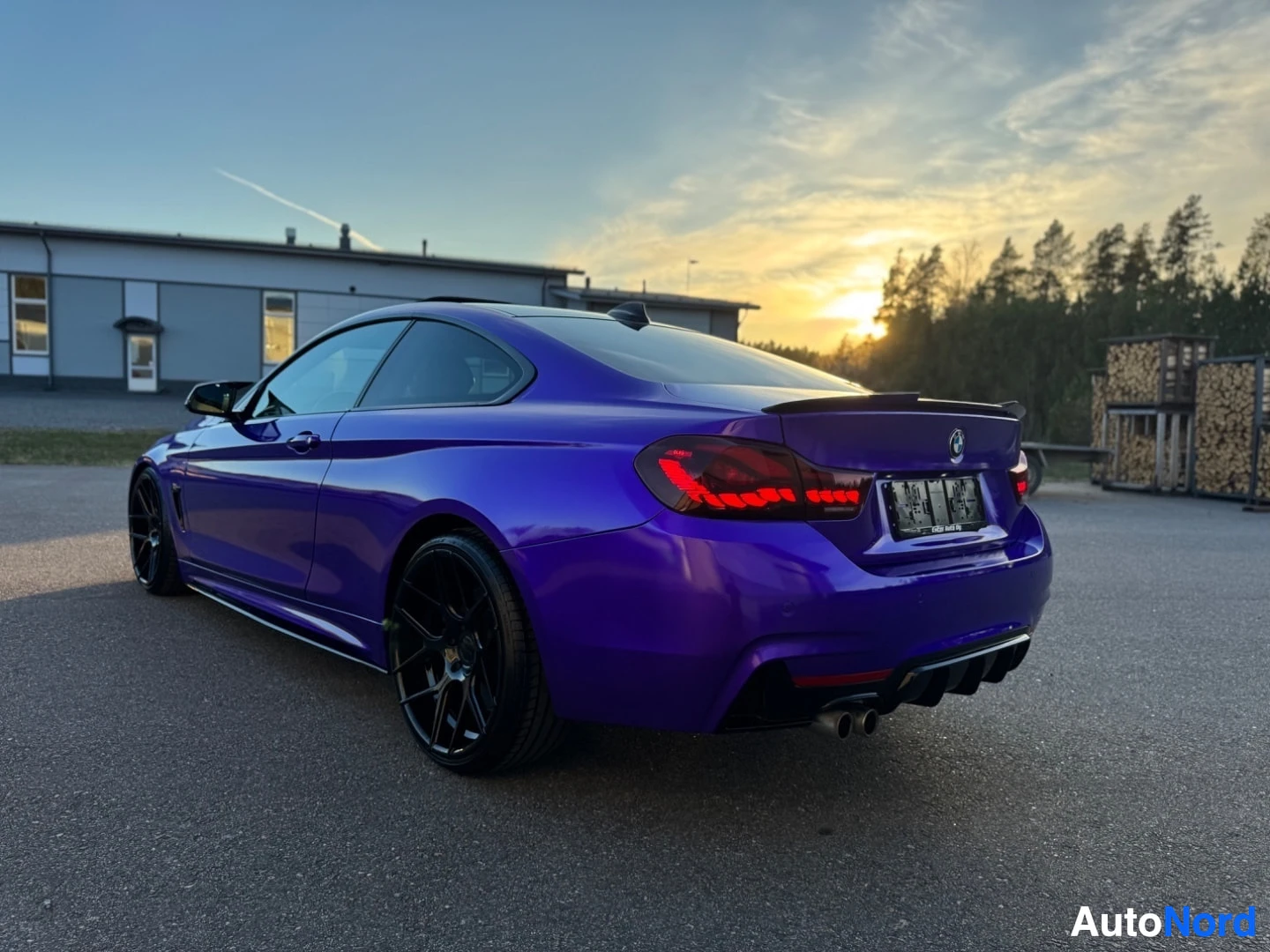 Takaviisto: Violetti kaksiovinen coupé-auto vasemmasta takaviistosta kuvattuna ulkona, auringonlaskun aikaan. Autossa on mustat monipuolaiset kevytmetallivanteet, mustat si