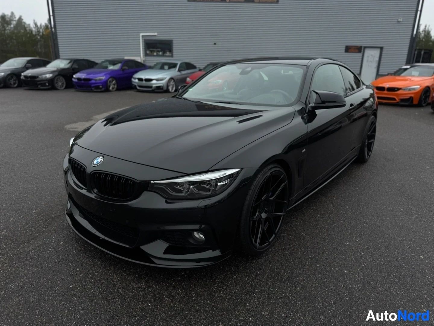 Etuviisto, nokka vasemmalle: Musta BMW 4-sarjan coupe pysäköitynä ulos autoliikkeen eteen, keula hieman vasemmalle ja etuosa kuvan keskellä.