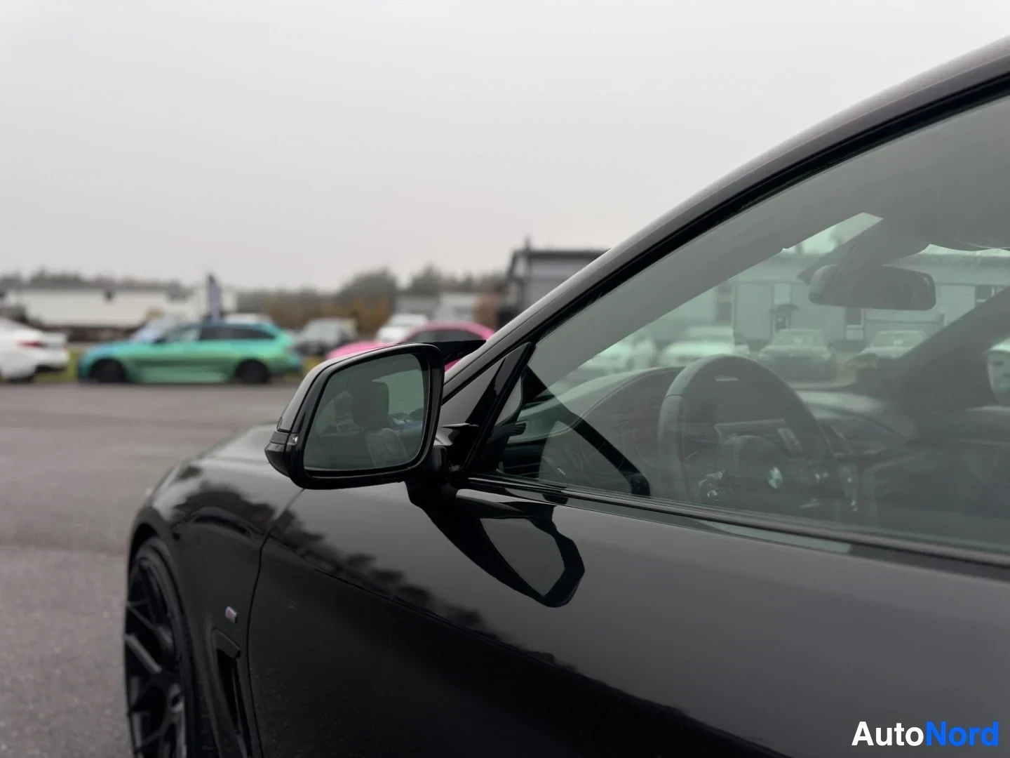 Yksityiskohta: Mustan auton sivupeili ja sivulasit. Peilistä heijastuu taustalla olevia autoja.