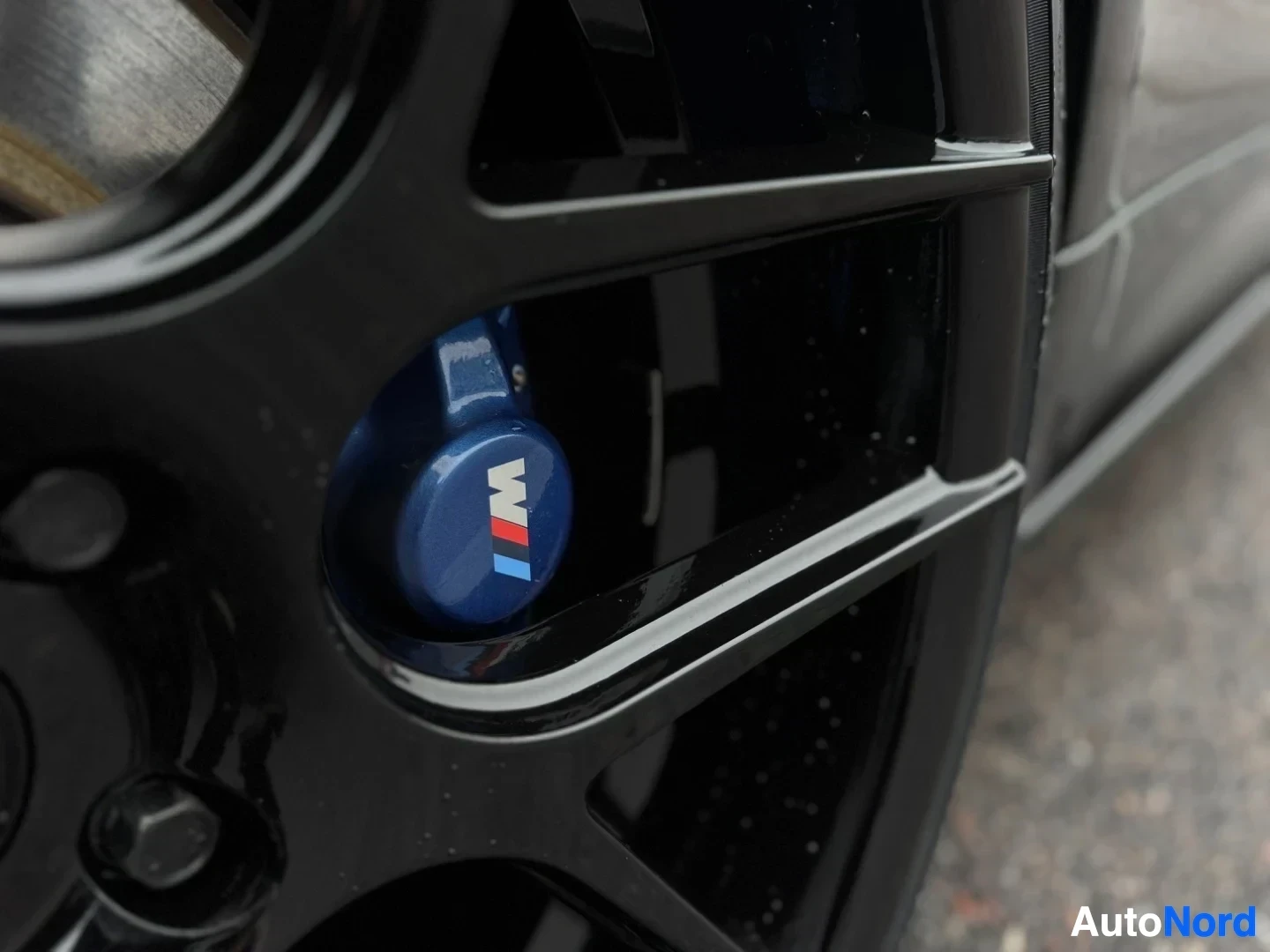 Yksityiskohta: Lähikuva mustasta kevytmetallivanteesta, jonka takana näkyy sininen jarrusatula BMW M -logolla.