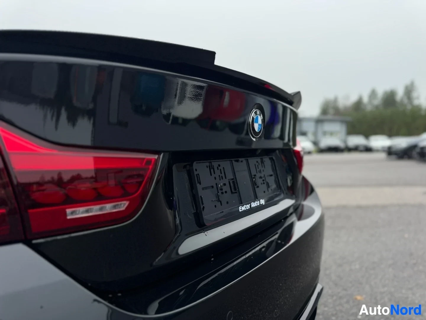 Takaviisto: Lähikuva auton takaosasta, jossa näkyy BMW-logo, tumma takaspoileri ja musta rekisterikilven pohja, jossa lukee "Ekstr- Auto Oy".