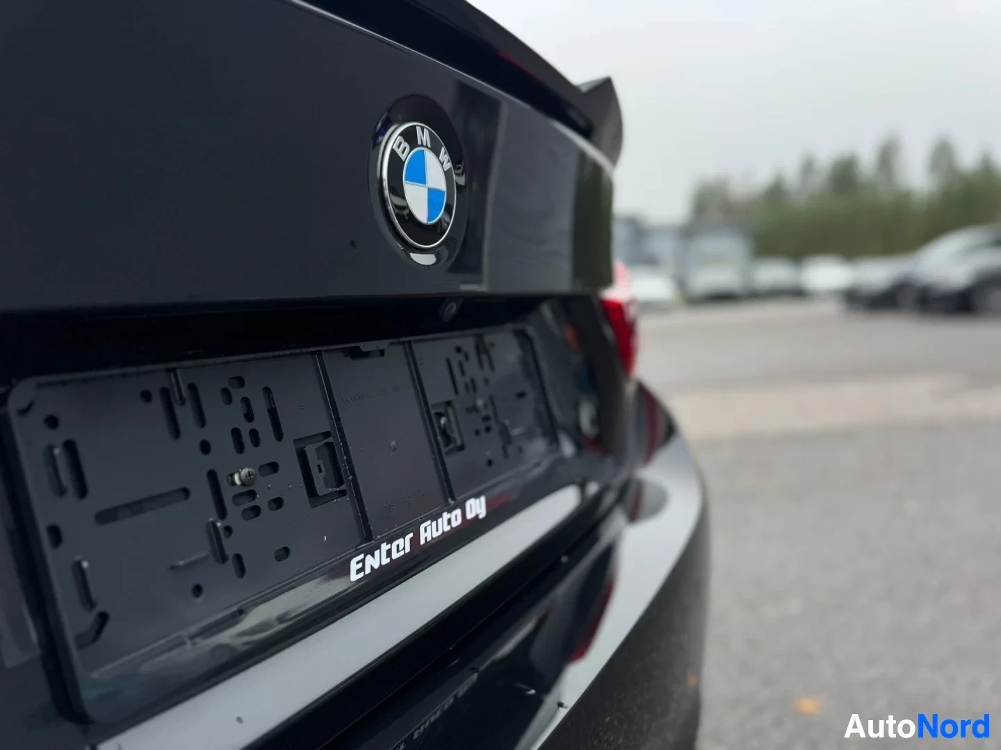 Takaviisto: Lähikuva auton takaosasta, jossa näkyvät BMW-logo, tavaratilan kansi ja rekisterikilven kehys tekstillä "Enter Auto Oy".