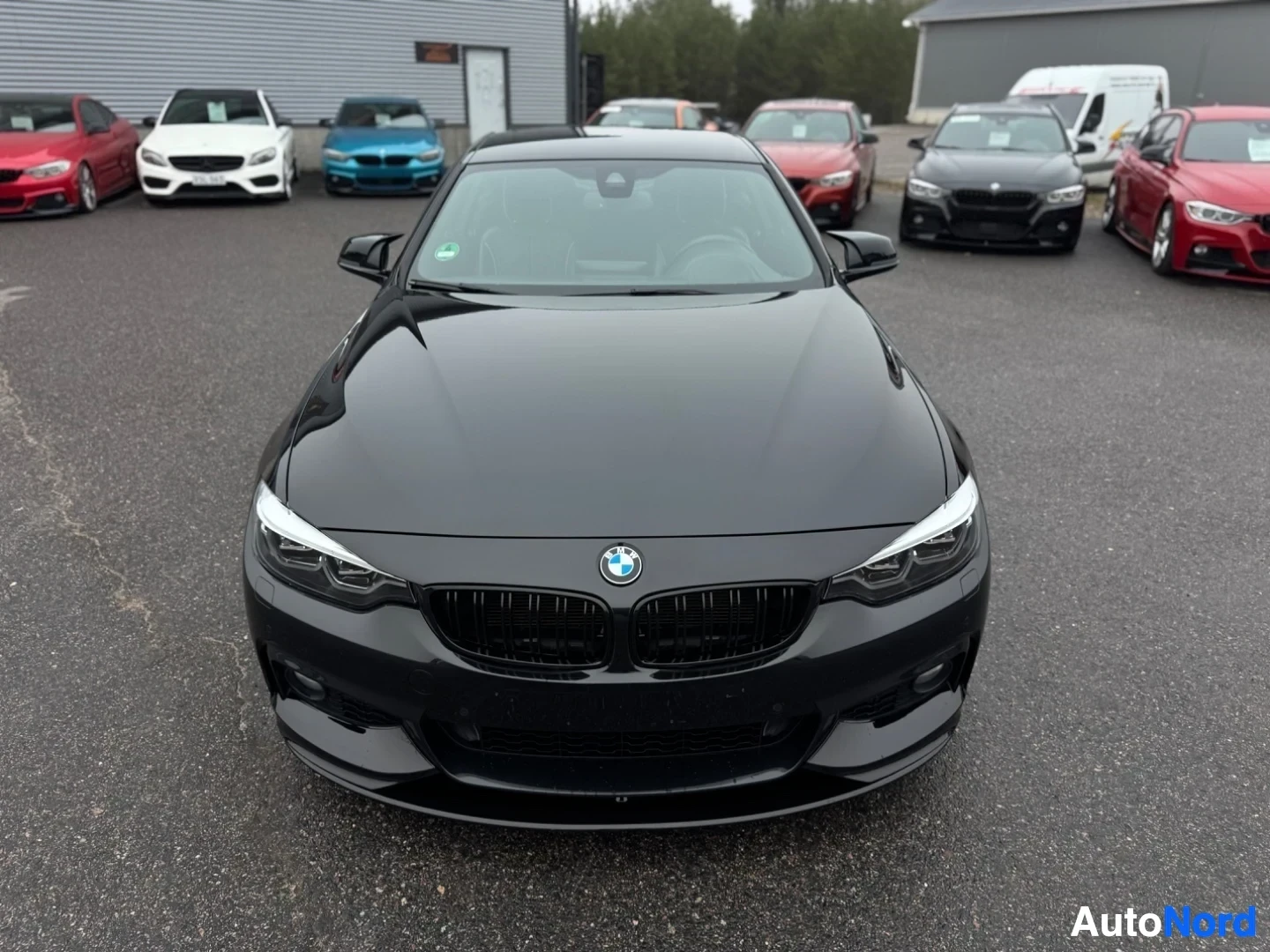 Edestä: Musta BMW 4-sarjan coupe edestä katsottuna, auto on pysäköitynä autoliikkeen eteen.