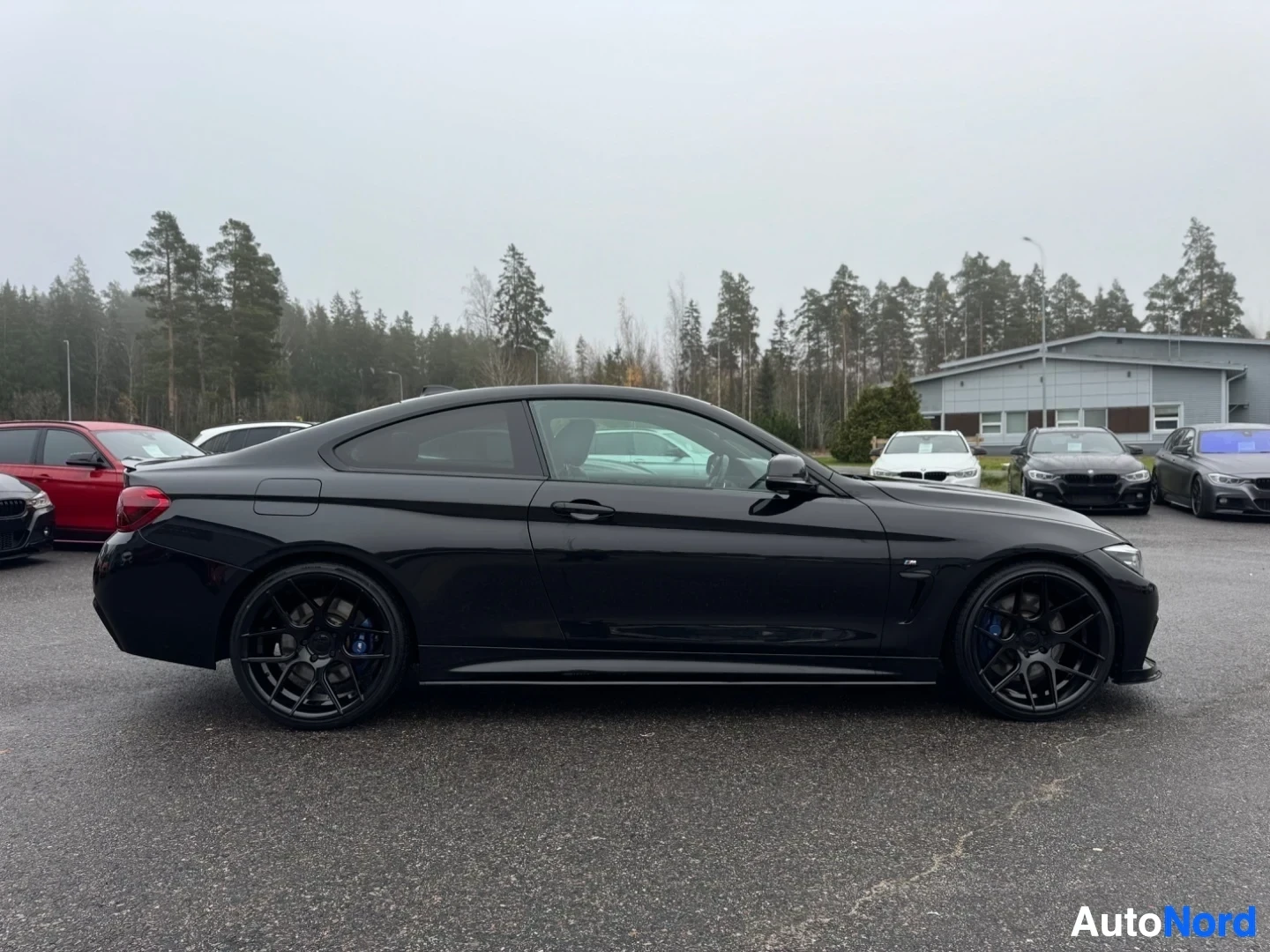 Sivulta: Musta coupé-auto sivusta kuvattuna oikealla puolella. Autossa on mustat kevytmetallivanteet ja siniset jarrusatulat näkyvissä.
