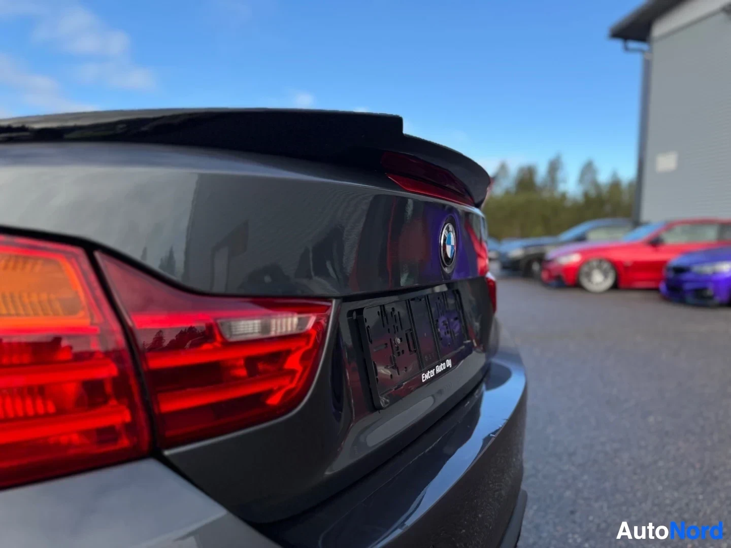 Takaviisto: Auton tummanharmaa takaosa vasemmasta takaviistosta. Takavalo näkyy vasemmalla, takakontissa on BMW-logo ja tyhjä rekisterikilven pidike, jossa lukee "Enter Aut