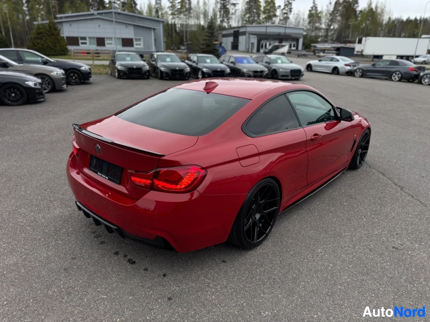 Takaviisto: Punainen BMW, joka on kuvattu takaoikealta, esittelee sen takapään ja kyljen, taustalla on useita muita autoja ja rakennuksia.