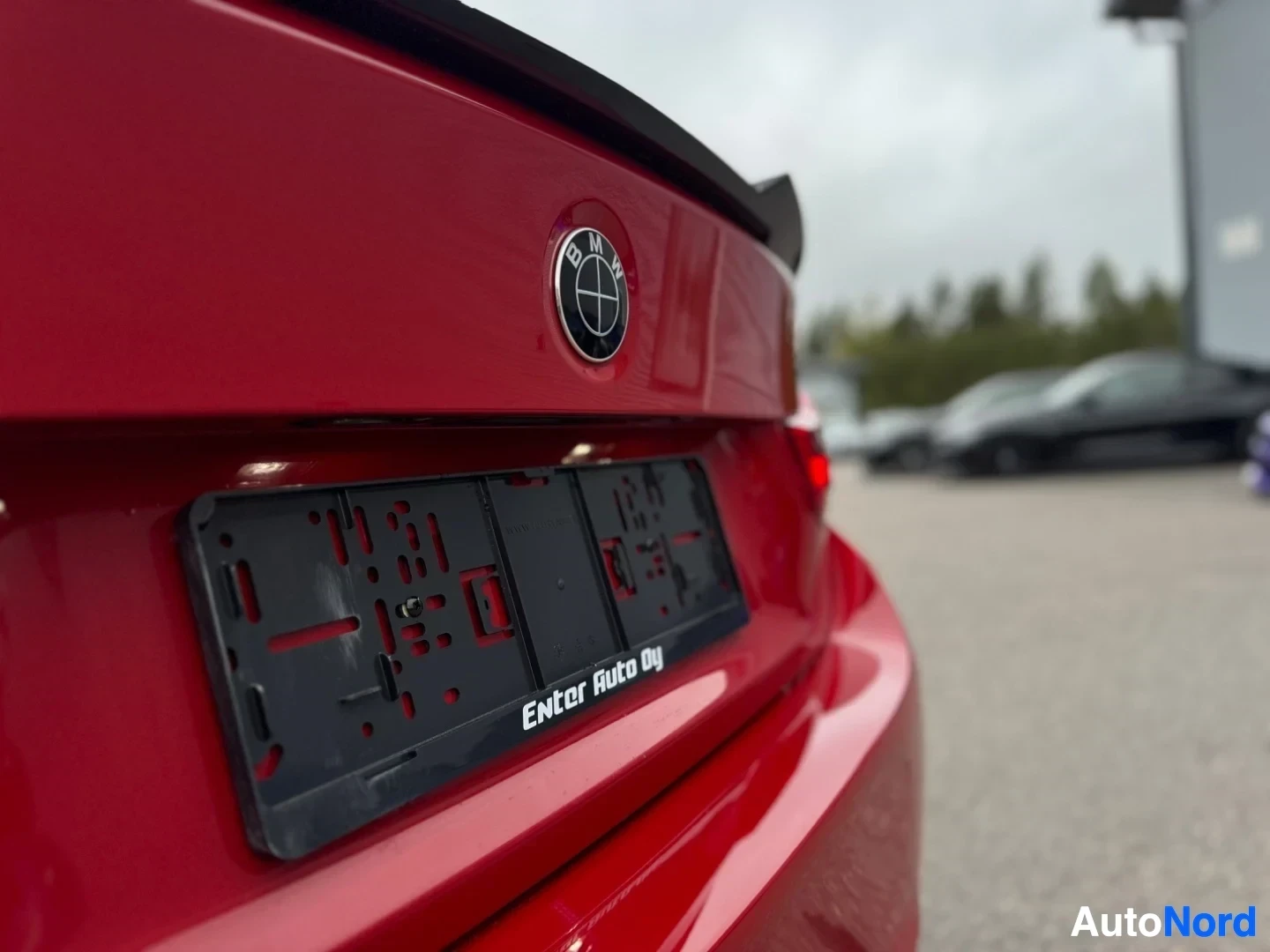 Takaviisto: Punaisen auton takaluukun keskiosa, jossa BMW-logo ja musta rekisterikilven teline tekstillä "ENter Auto Oy".