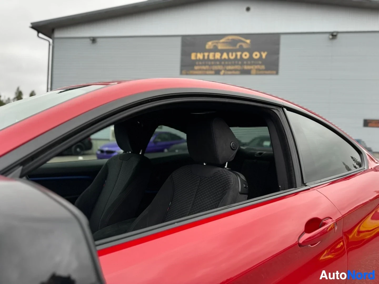 Ohjaamo: Punaisen coupé-auton oikea kylki, ikkunat ja sisätilan etuistuimet näkyvissä. Taustalla rakennus, jossa kyltti "ENTERAUTO OY".