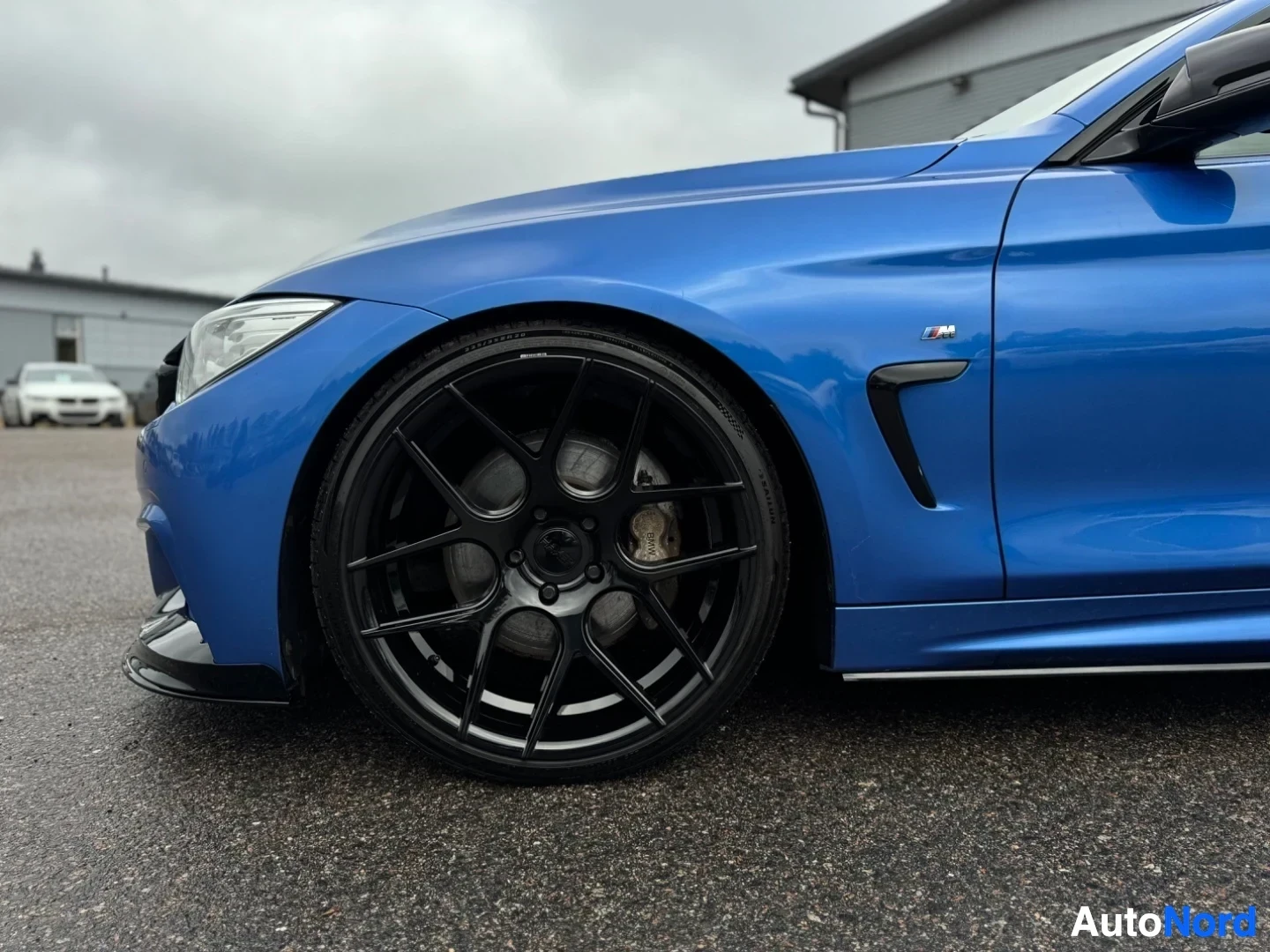 Yksityiskohta: Lähikuva auton etupyörästä ja etulokasuojasta. Autossa on musta, monipuolainen kevytmetallivanne ja BMW M-logo lokasuojan tuuletusaukon yläpuolella.