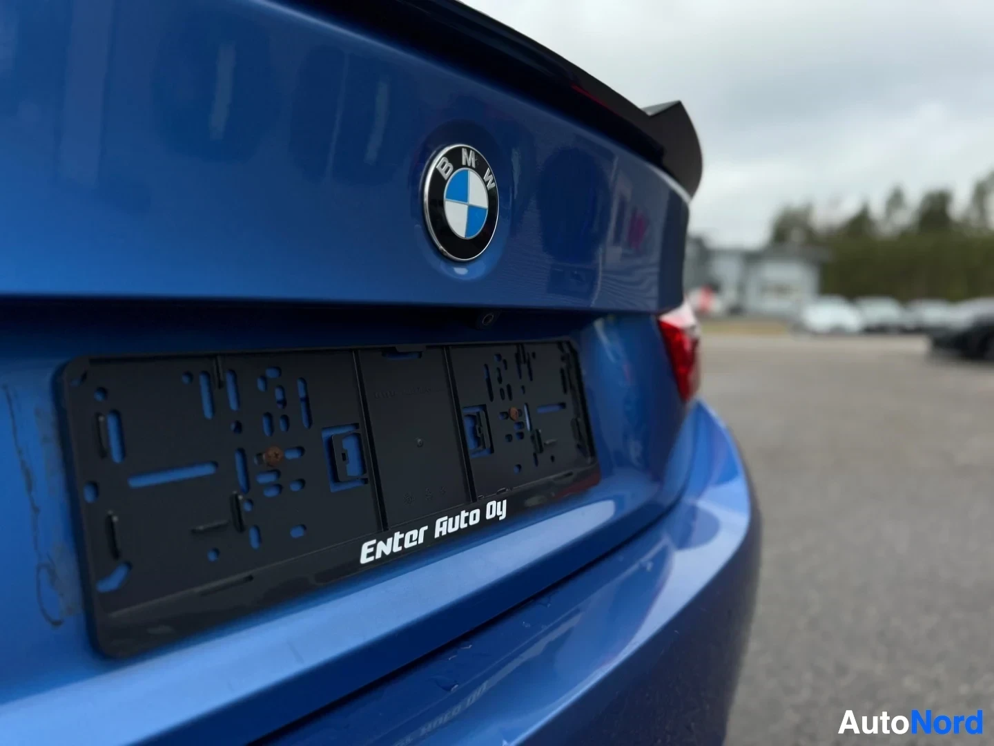 Takaa: Lähikuva auton sinisestä takapäästä, jossa BMW-logo, takasiipi ja rekisterikilven pohja tekstillä "Enter Auto Oy".