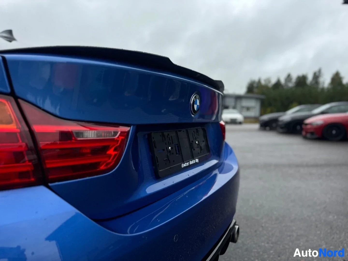 Takaviisto: Lähikuva sinisen auton perästä. Näkyvissä on takavalot, musta takaspoileri, takaluukun BMW-logo ja tyhjä rekisterikilven pidike, jossa lukee "Ewelter Auto Oy".