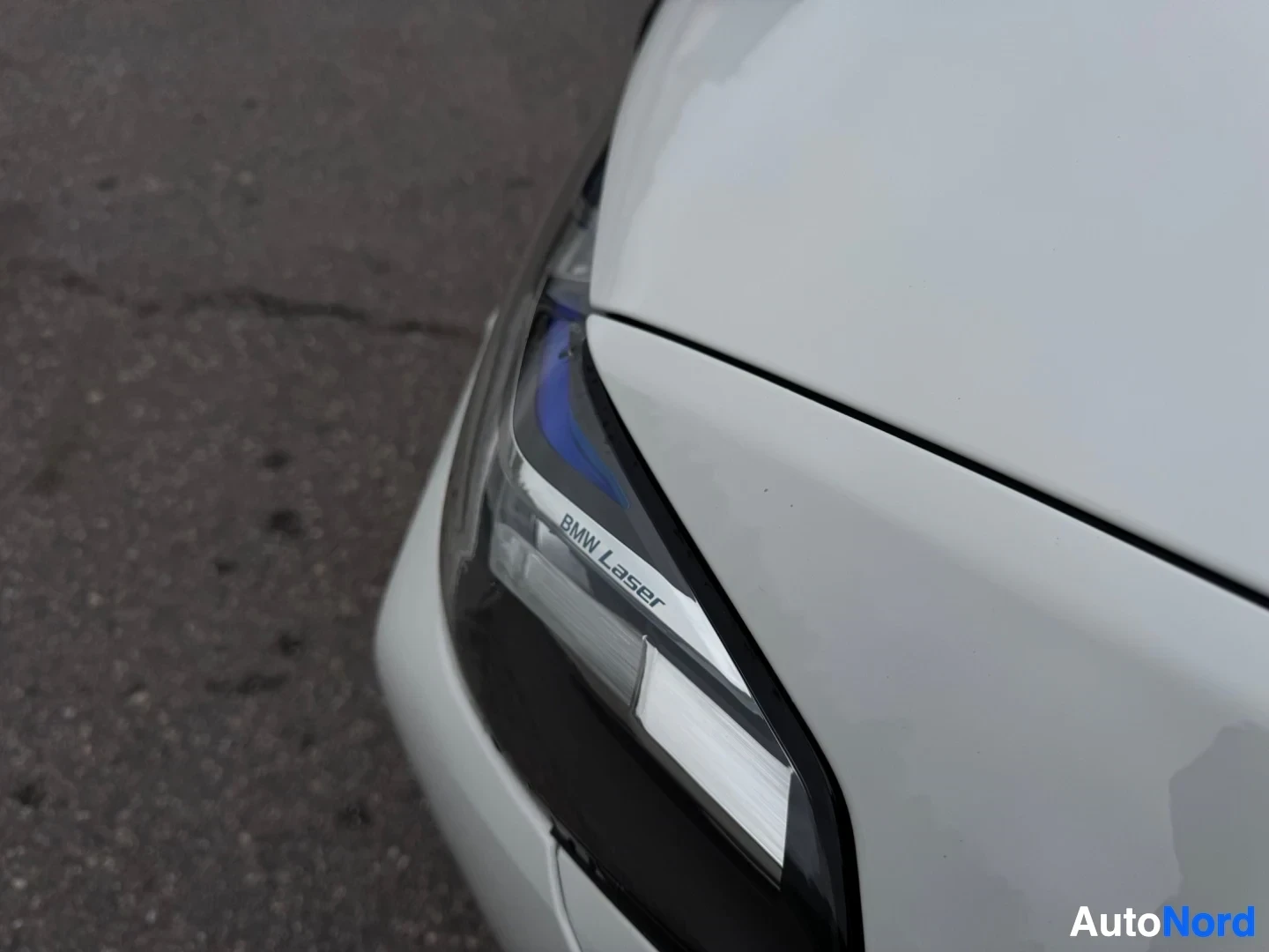 Yksityiskohta: Lähikuva valkoisen auton etuosasta, jossa näkyy oikea etuvalo. Ajovalon sisällä lukee "BMW Laser".