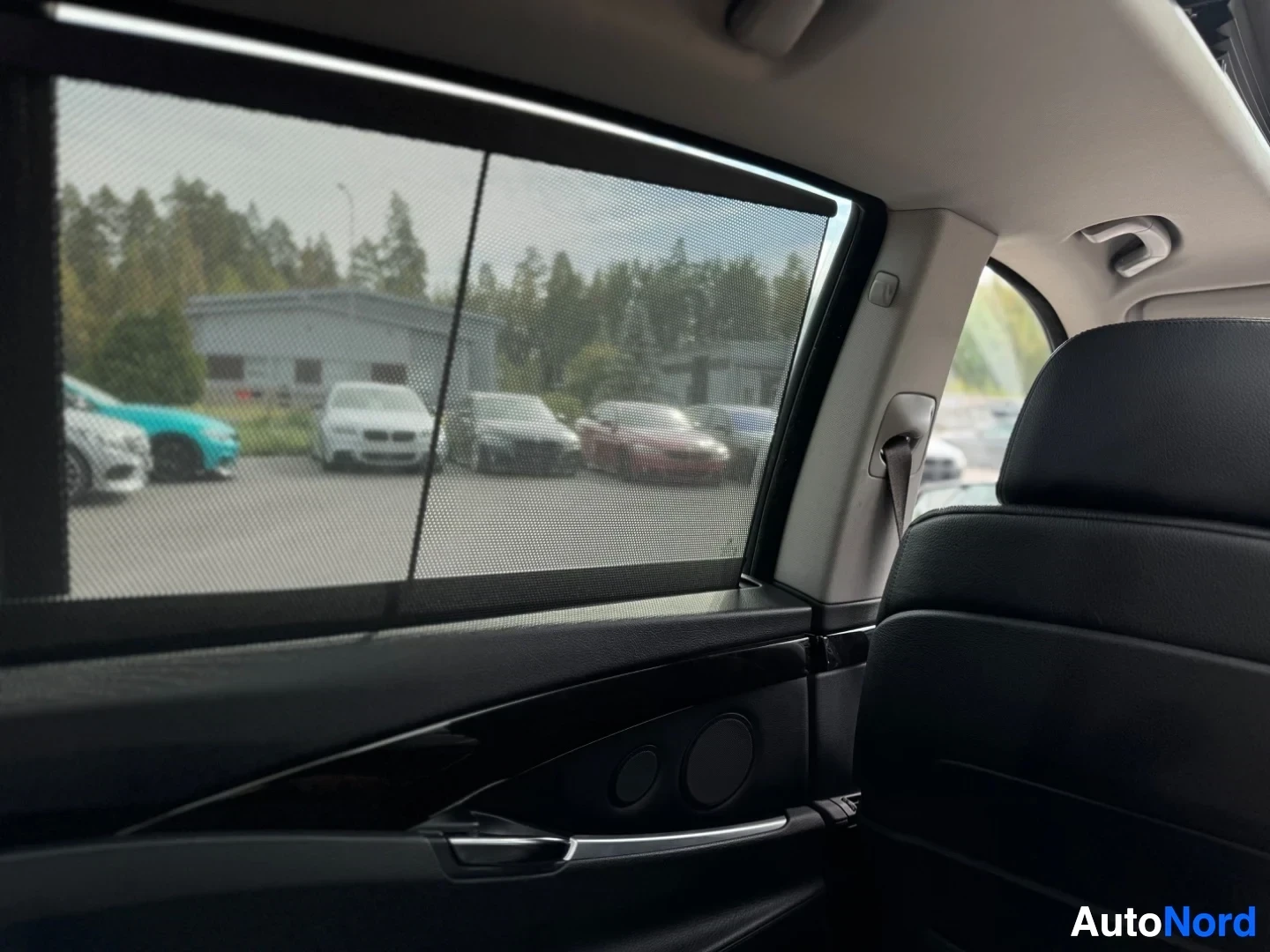 Ohjaamo: Kuva auton takasivulaseista, joissa on aurinkoverhot, näkymä auton ulkopuolelle pysäköityihin autoihin.