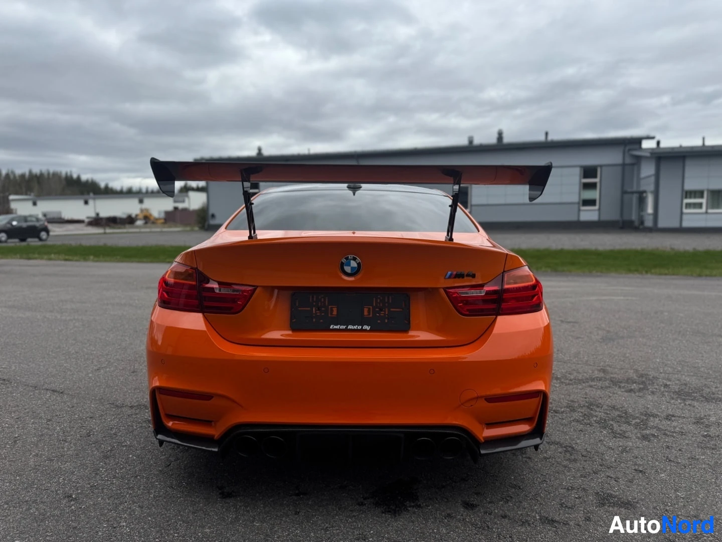 Takaa: Oranssi BMW M4 suoraan takaa. Autossa on iso takasiipi ja neljä pakoputkenpäätä. Rekisterikilvessä teksti 'Eviter Auto Oy'.
