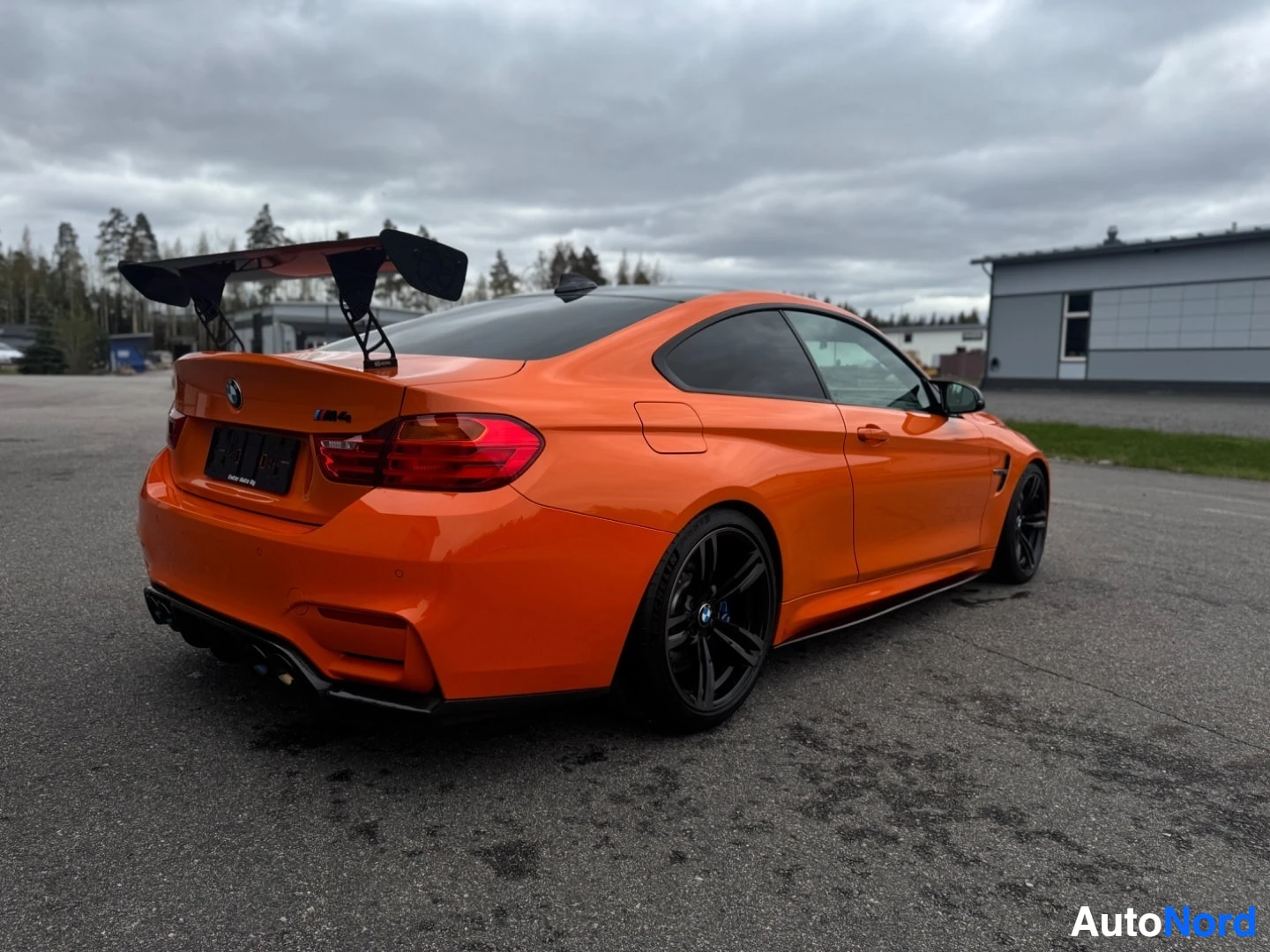 Takaviisto: Oranssi BMW M4 takaviistosta, iso takasiipi ja mustat vanteet. Takavalot ja oikea kylki näkyvissä.