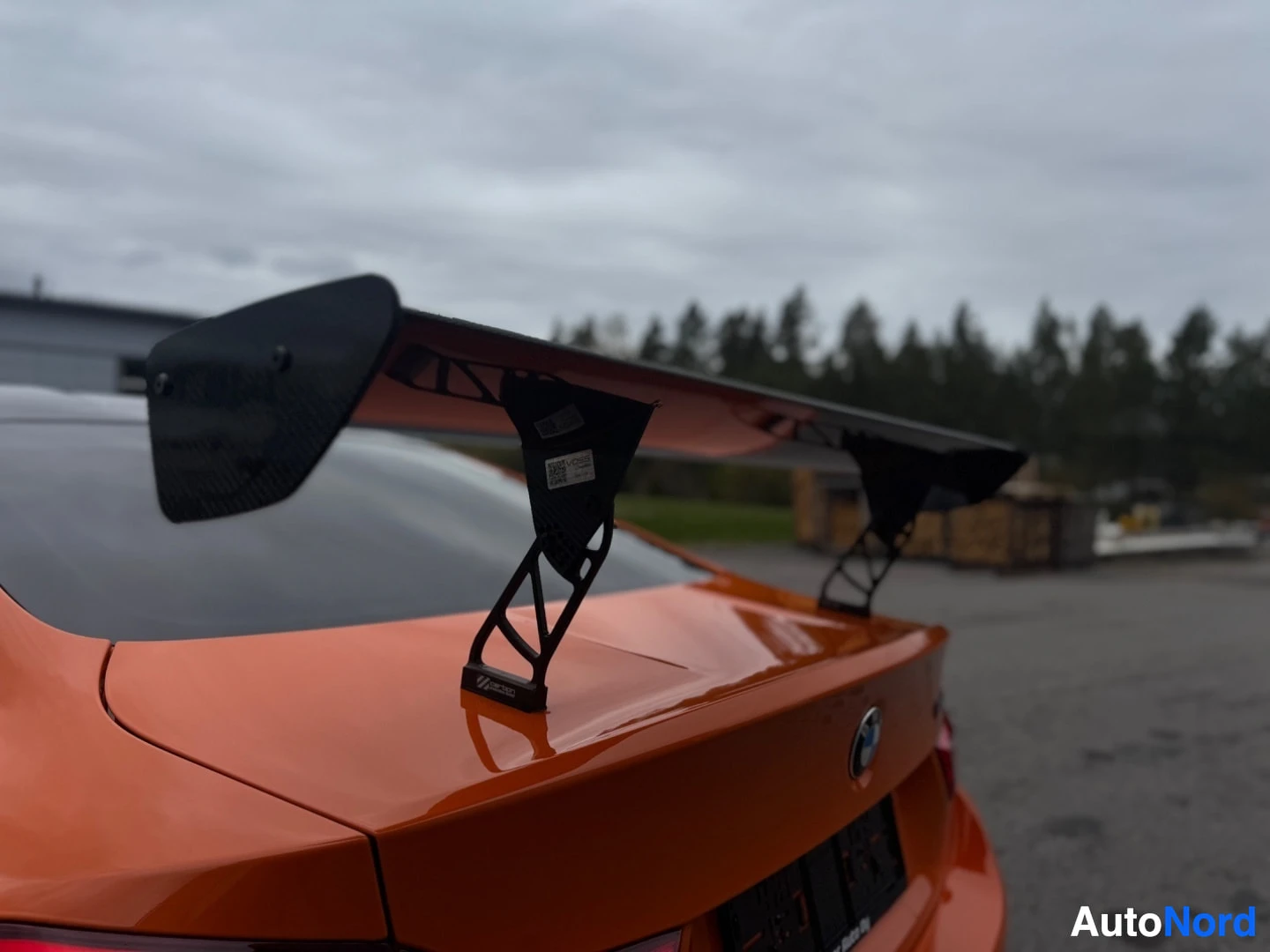 Takaviisto: Lähikuva auton takaosasta, jossa näkyy suuri, musta takaspoileri, takaosa ja takalasi. Spoilerin kiinnitysjalassa on tarra, jossa lukee "M4 GT4".