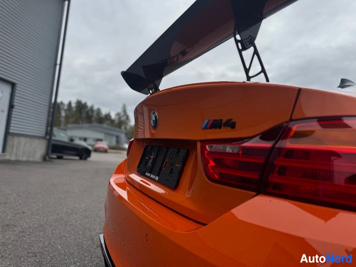 Takaviisto: Lähikuva auton takaosasta, jossa näkyy "M4"-merkki takaluukussa, oikeanpuoleinen takavalo ja osittain musta rekisterikilven alusta, jossa lukee "Enter Auto Oy".