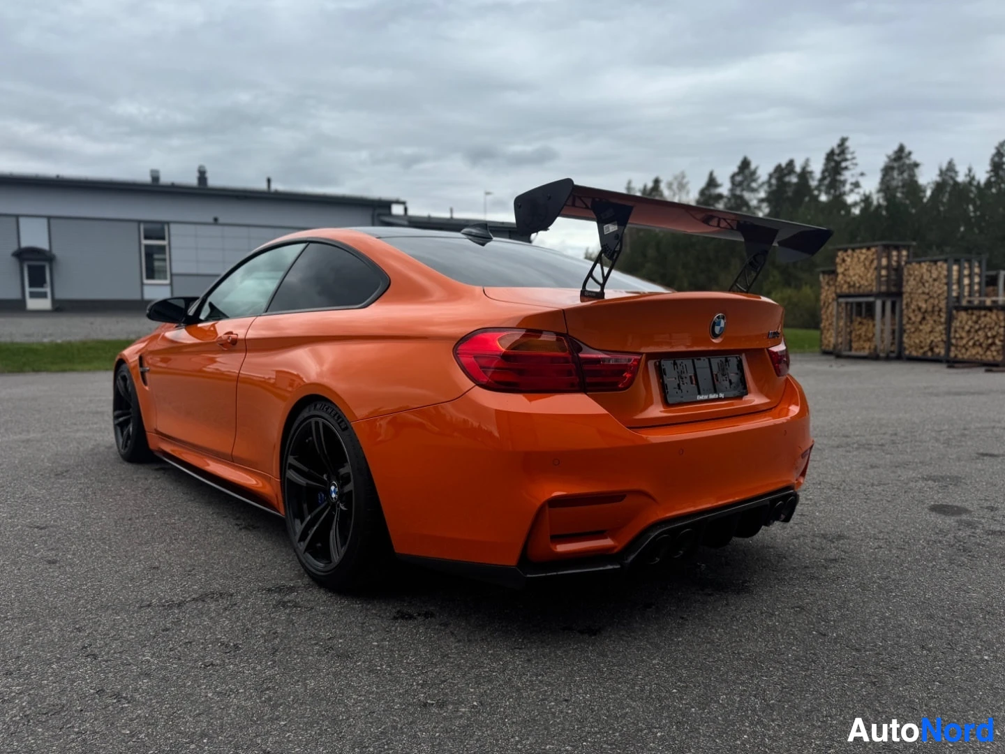 Takaviisto: Oranssi BMW M4 takaviistosta, iso takasiipi ja mustat vanteet. Takavalot ja vasen kylki näkyvissä.