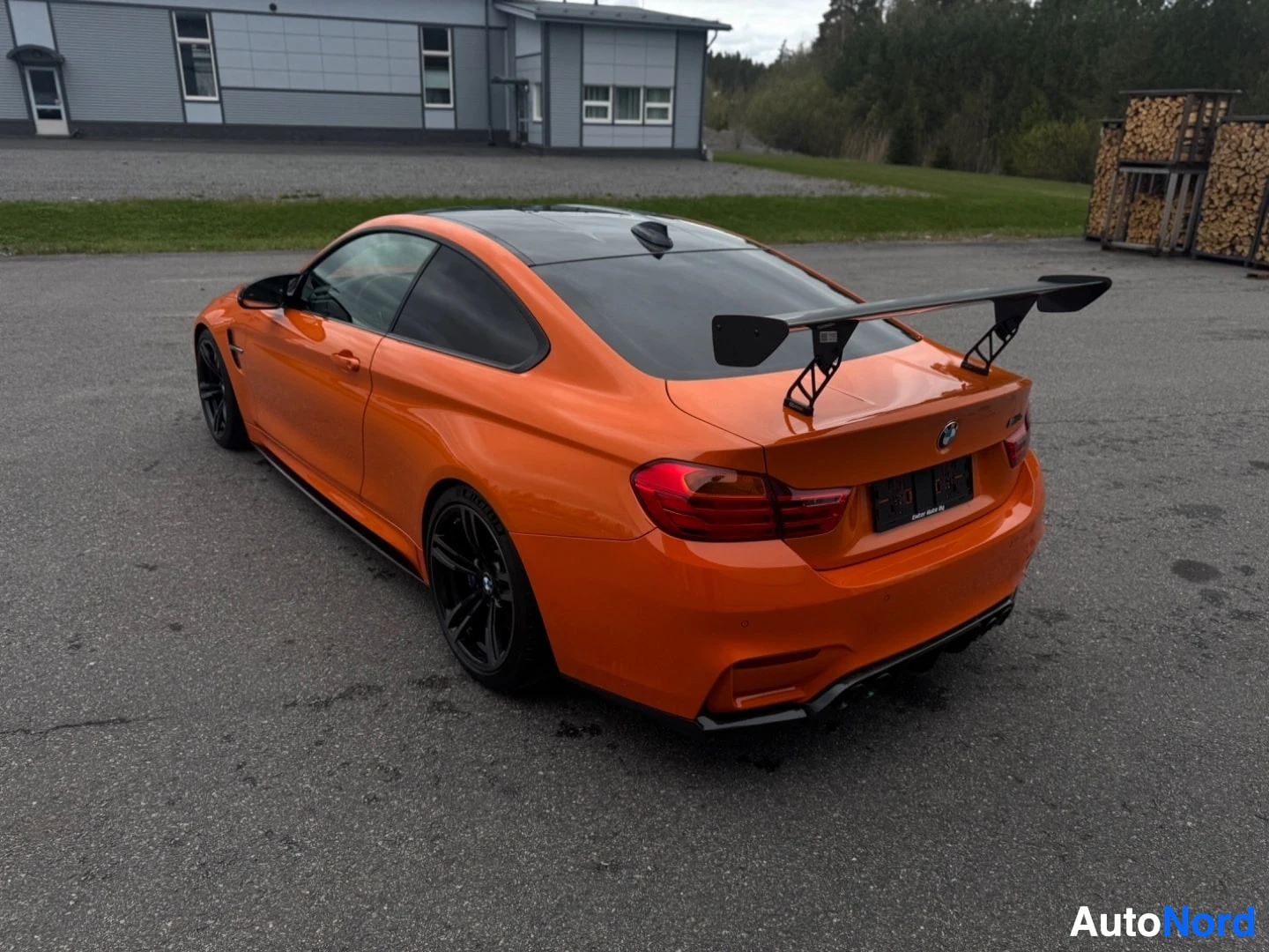 Takaviisto: Oranssi BMW M4 takaviistosta, iso takasiipi ja mustat vanteet. Takavalot ja oikea kylki näkyvissä.