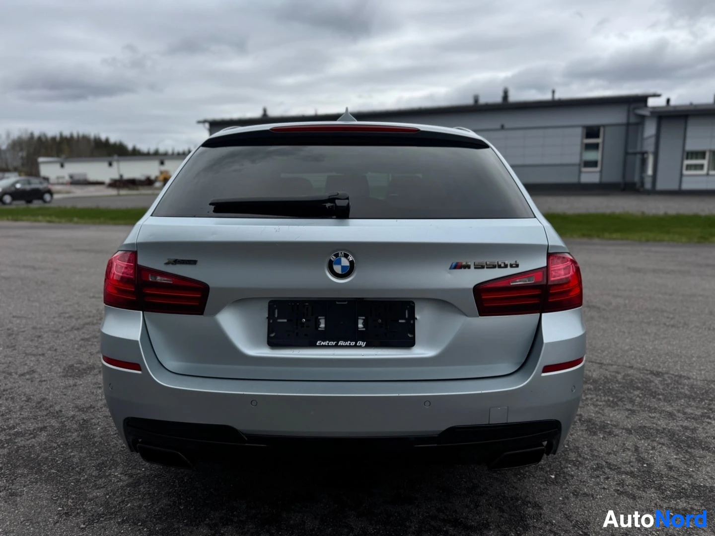 Takaa: Hopeanvärinen BMW 5-sarjan farmari kuvattuna suoraan takaa. Näkyvissä ovat takapuskuri, takaluukku, takavalot ja rekisterikilven paikka. Takaluukussa lukee 'M55