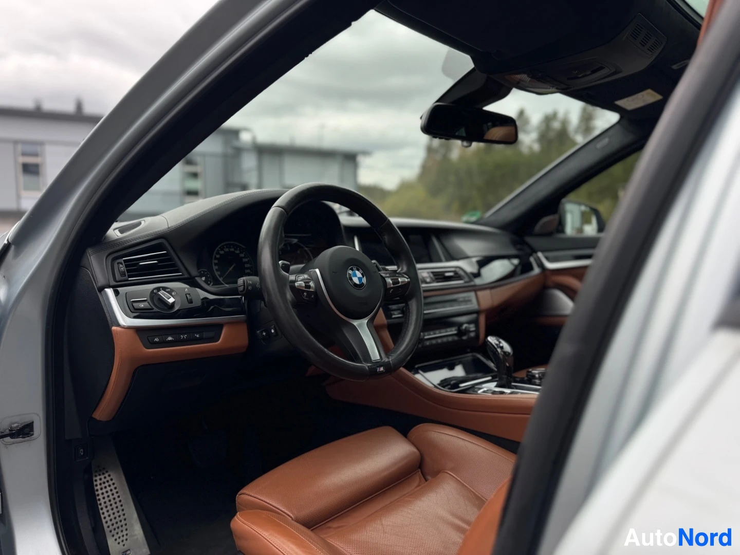 Ohjaamo: Kuskin oven ollessa auki, näkyy ohjauspyörä, kojelauta, keskikonsoli ja ruskea matkustajan istuin kuljettajan puolelta kuvattuna.
