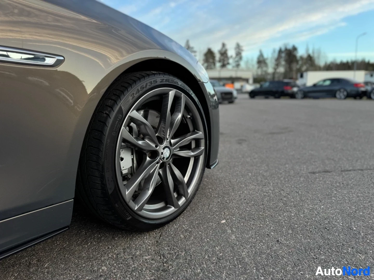 Yksityiskohta: Auton etupyörän ja sivupaneelin lähikuva, kuvattu matalasta kulmasta. Renkaassa lukee Pirelli P Zero ja koko on 245/35 ZR20. Keskellä vannetta on BMW-logo.